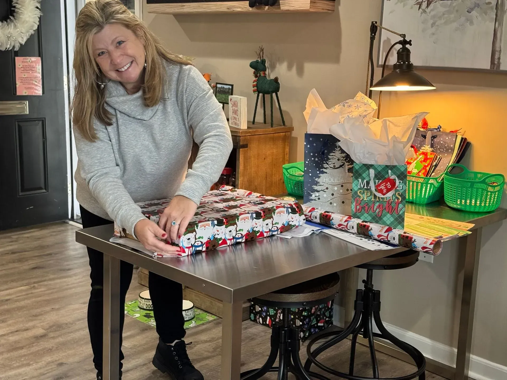 Woman beside a table of small holiday crafts and gift baskets in a kitchen.