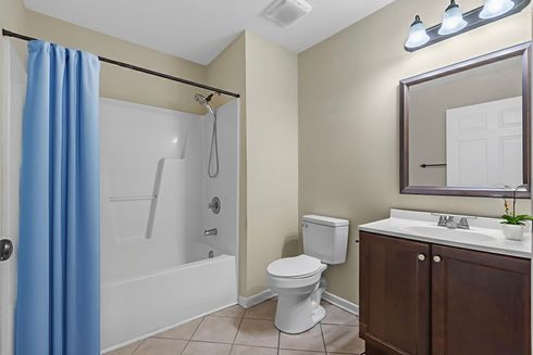 Bright bathroom with tub shower, toilet, vanity sink, and blue shower curtain