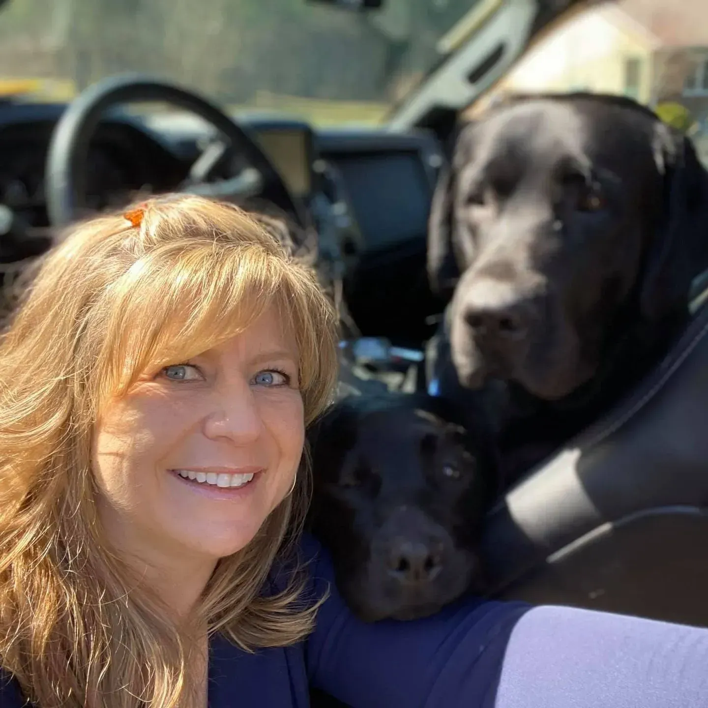 Woman smiling in a car with two black dogs, one large and one small, in the front seat
