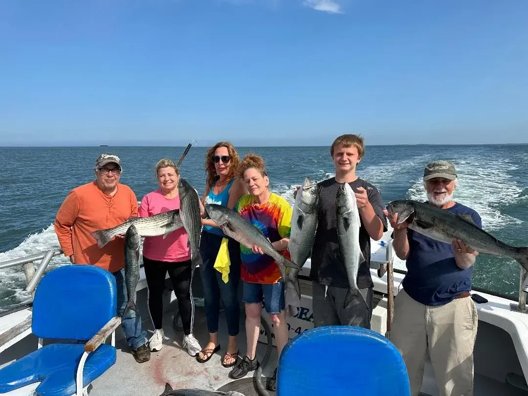 Six people on a boat holding fish, with open water and blue sky behind them.