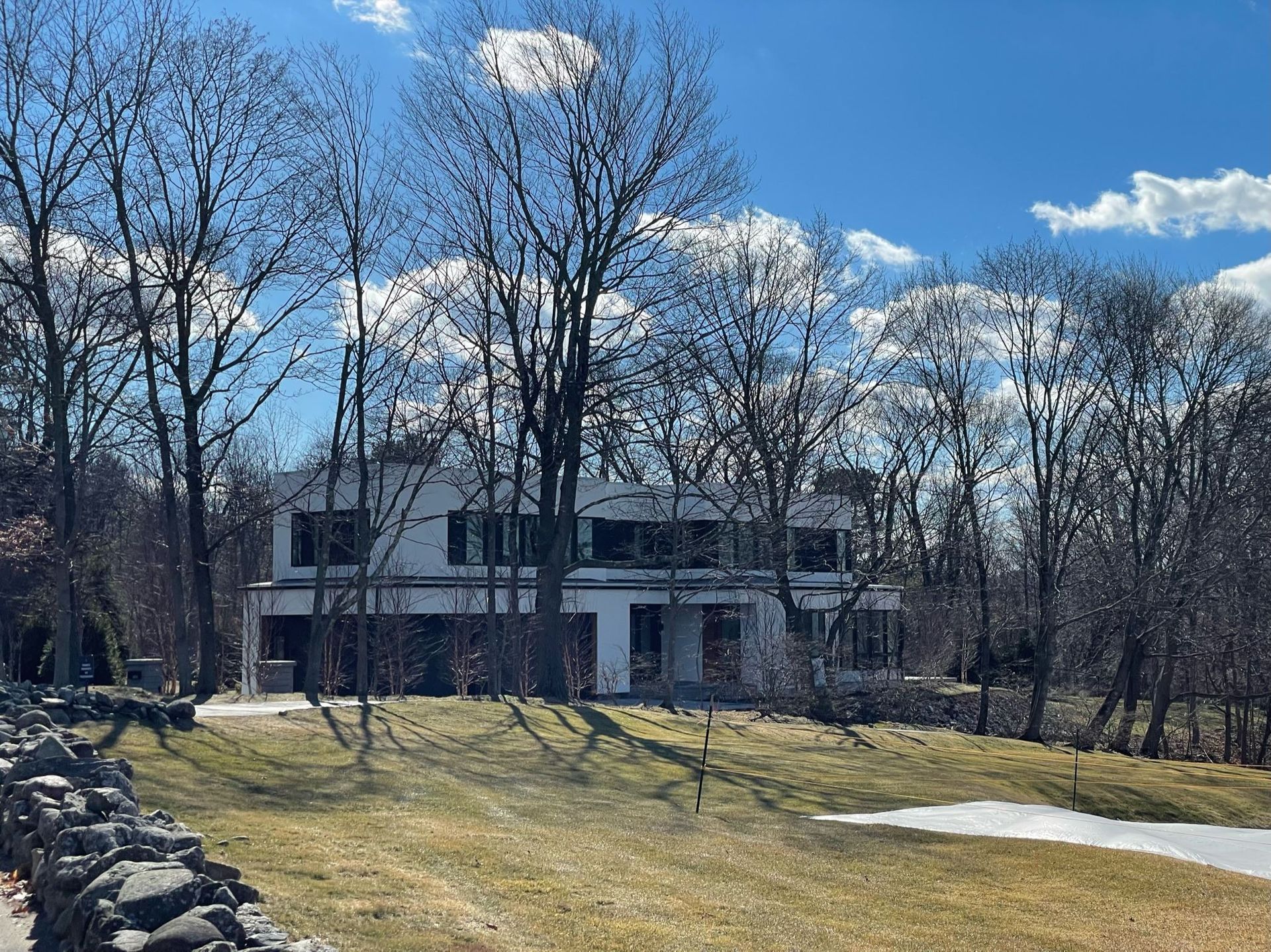 A large white house is surrounded by trees on a sunny day.