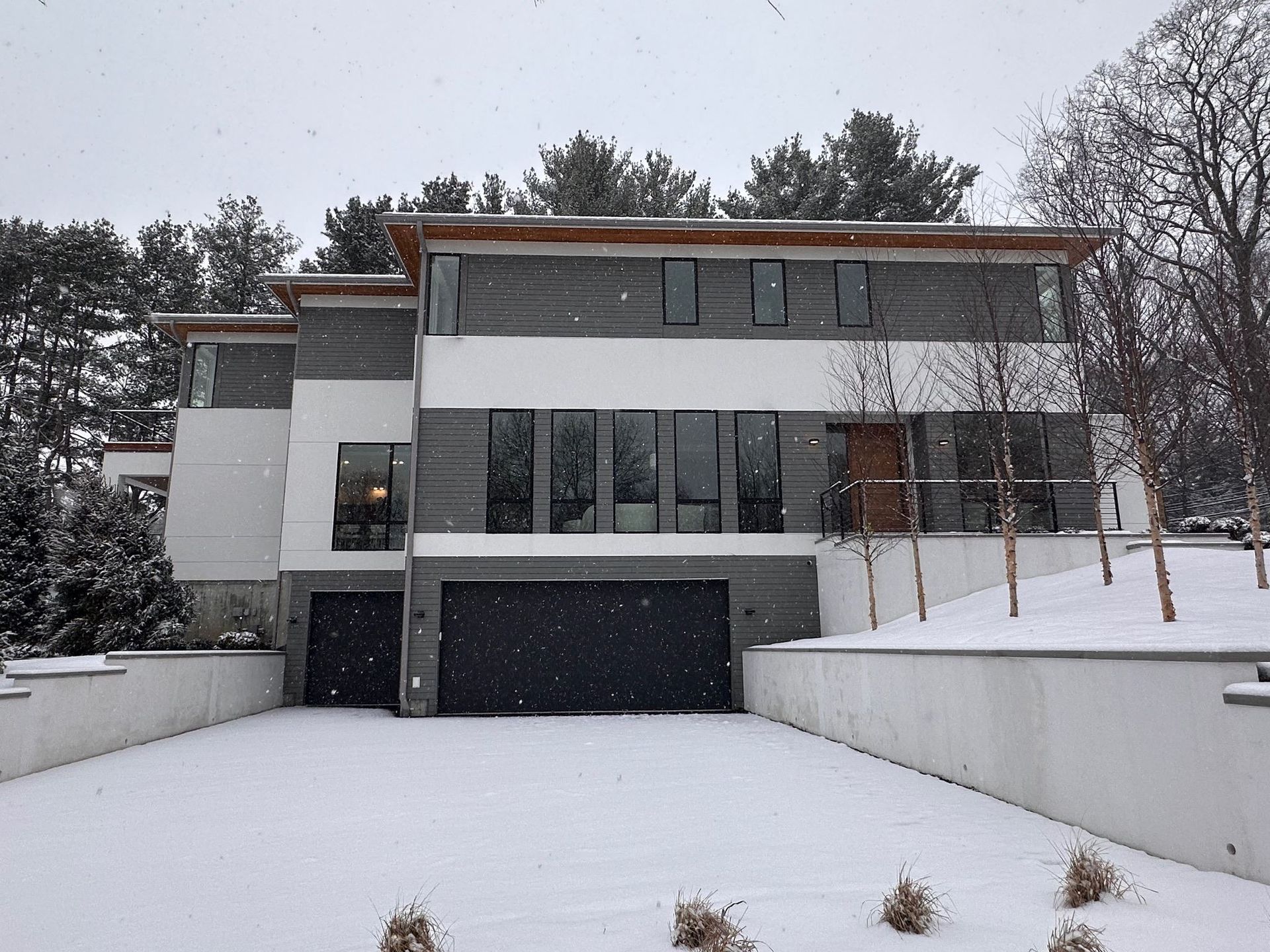 A large house with a black garage door is covered in snow