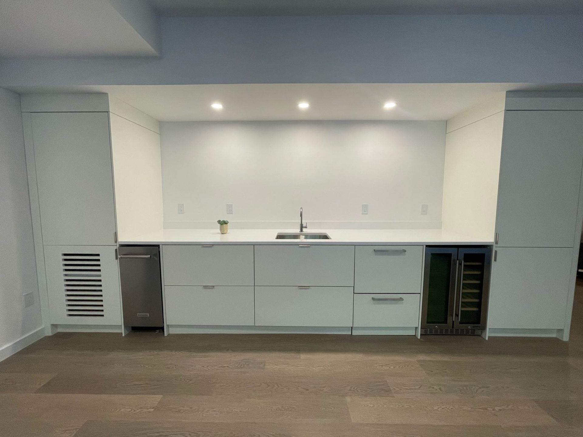 A kitchen with white cabinets , a sink , and a wine cooler.