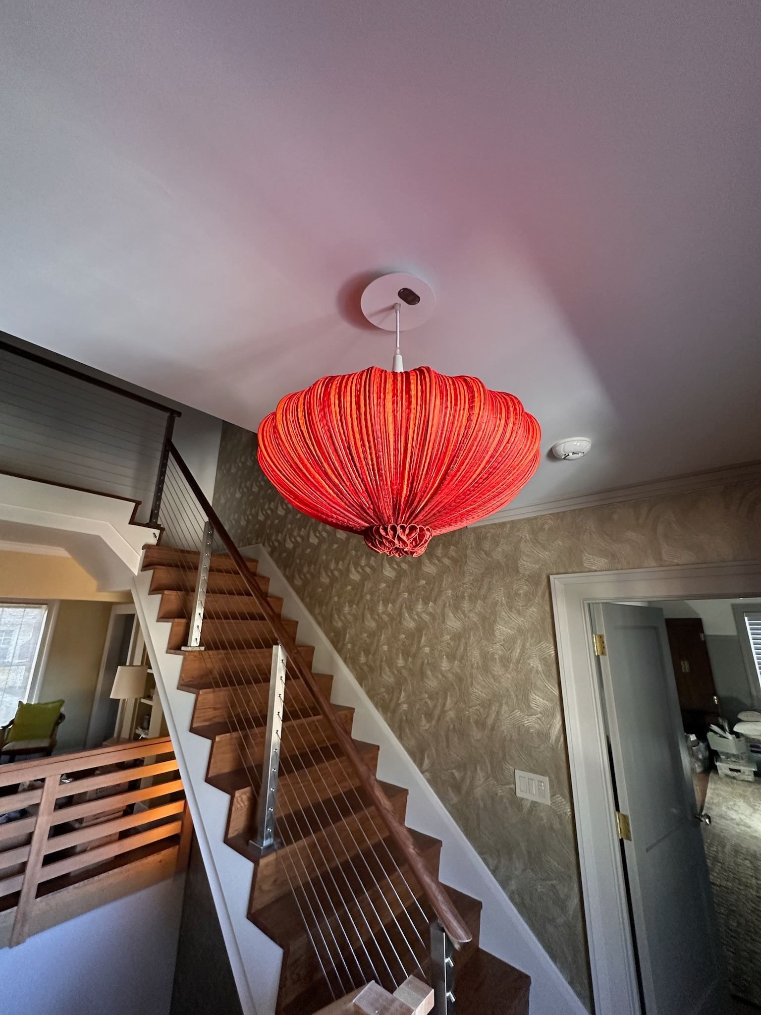 A red chandelier is hanging from the ceiling above a wooden staircase.