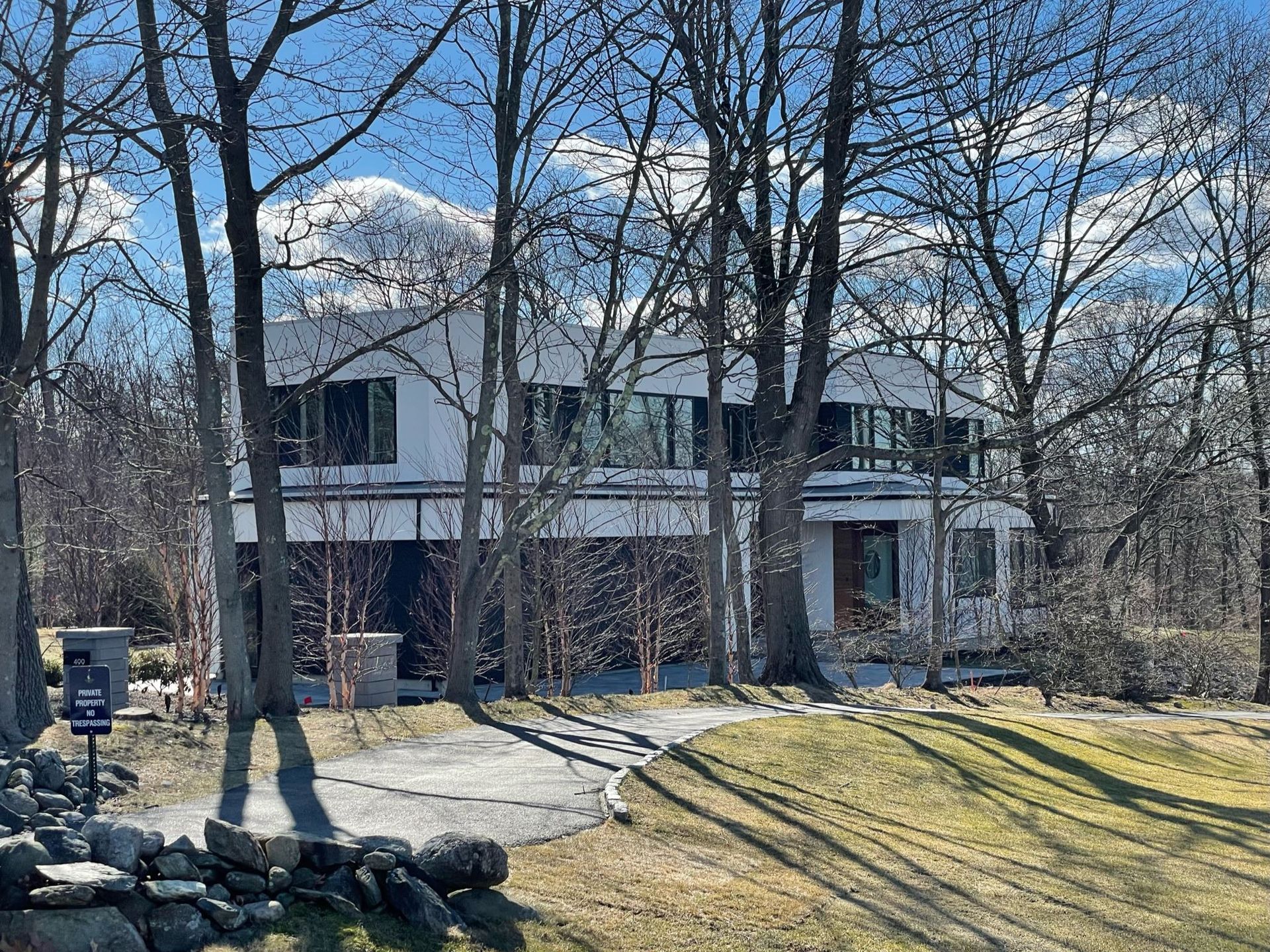 A large white house is surrounded by trees on a sunny day.