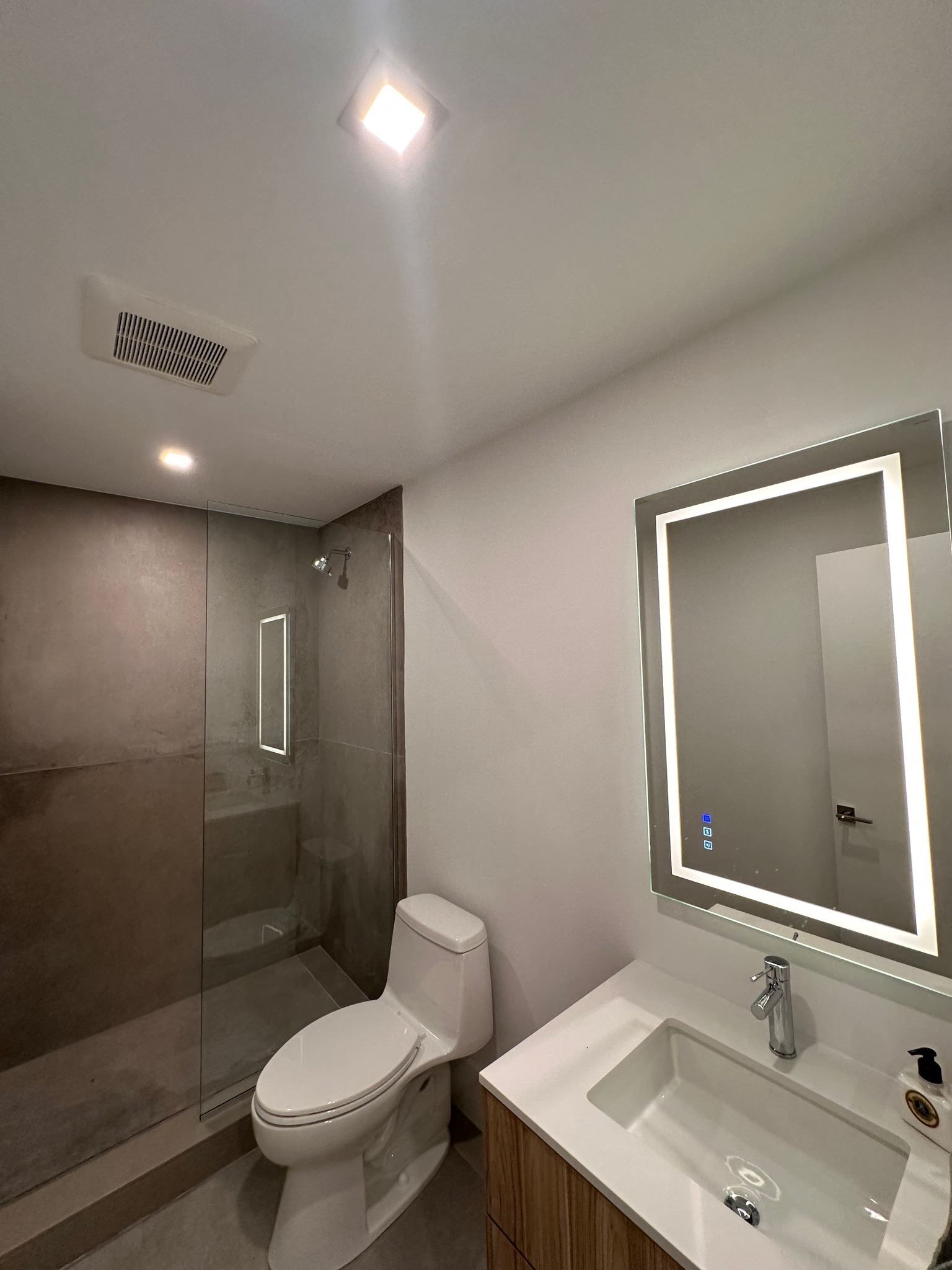 A bathroom with a toilet , sink , shower and mirror.