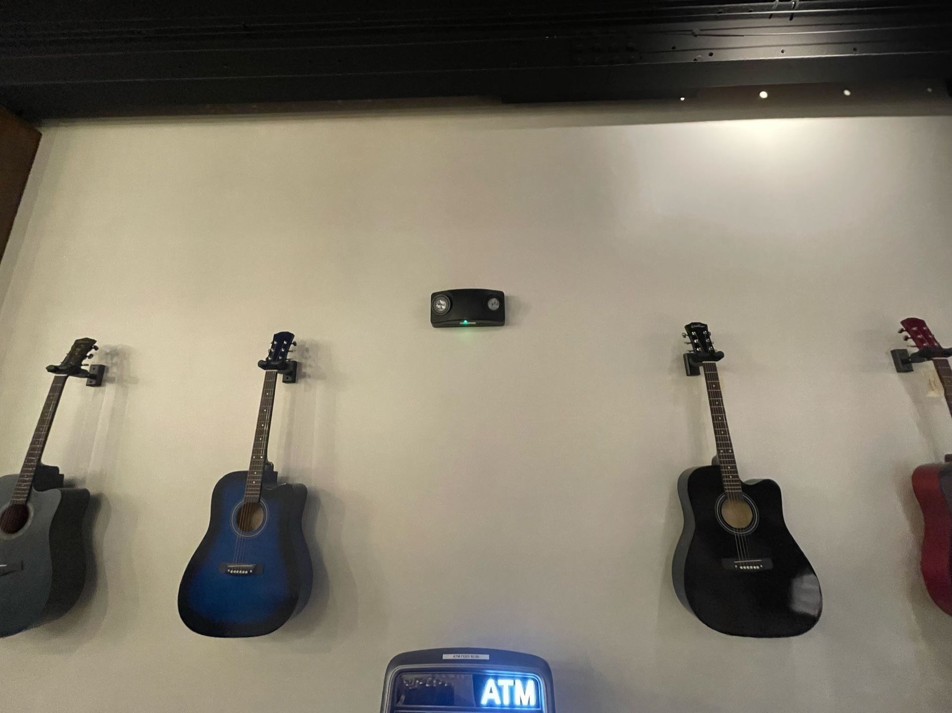 Four guitars are hanging on a wall next to an atm machine