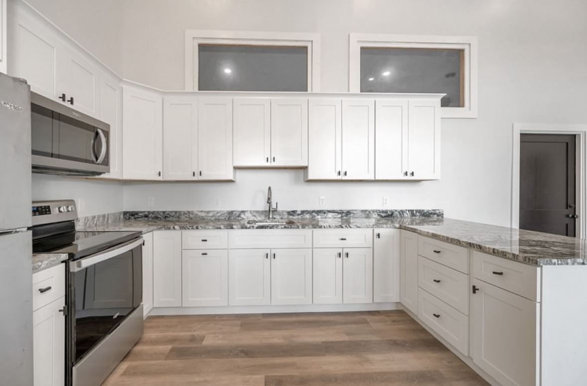 A kitchen with white cabinets , stainless steel appliances , and granite counter tops.