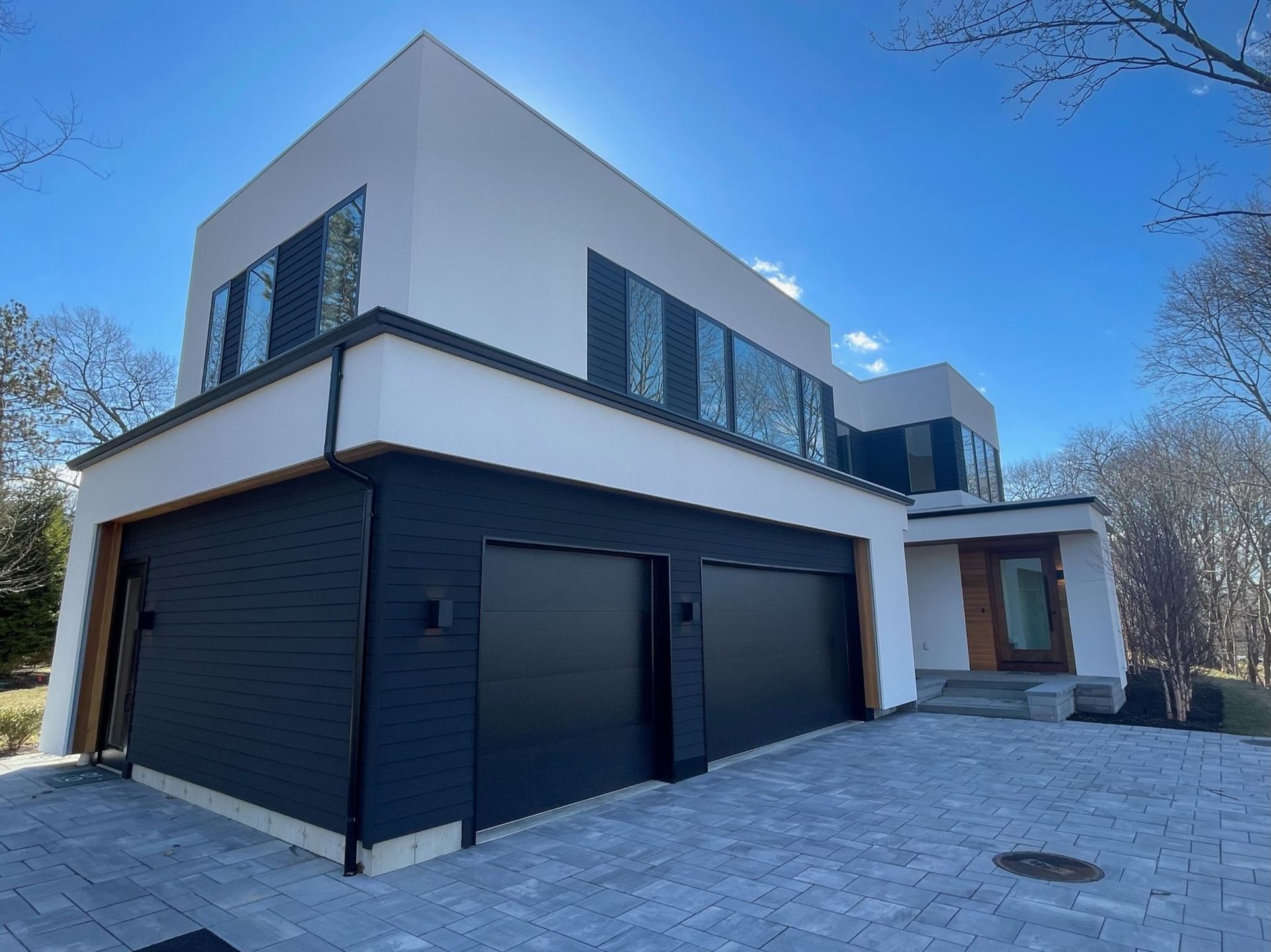 A modern house with a black garage door and a brick driveway.