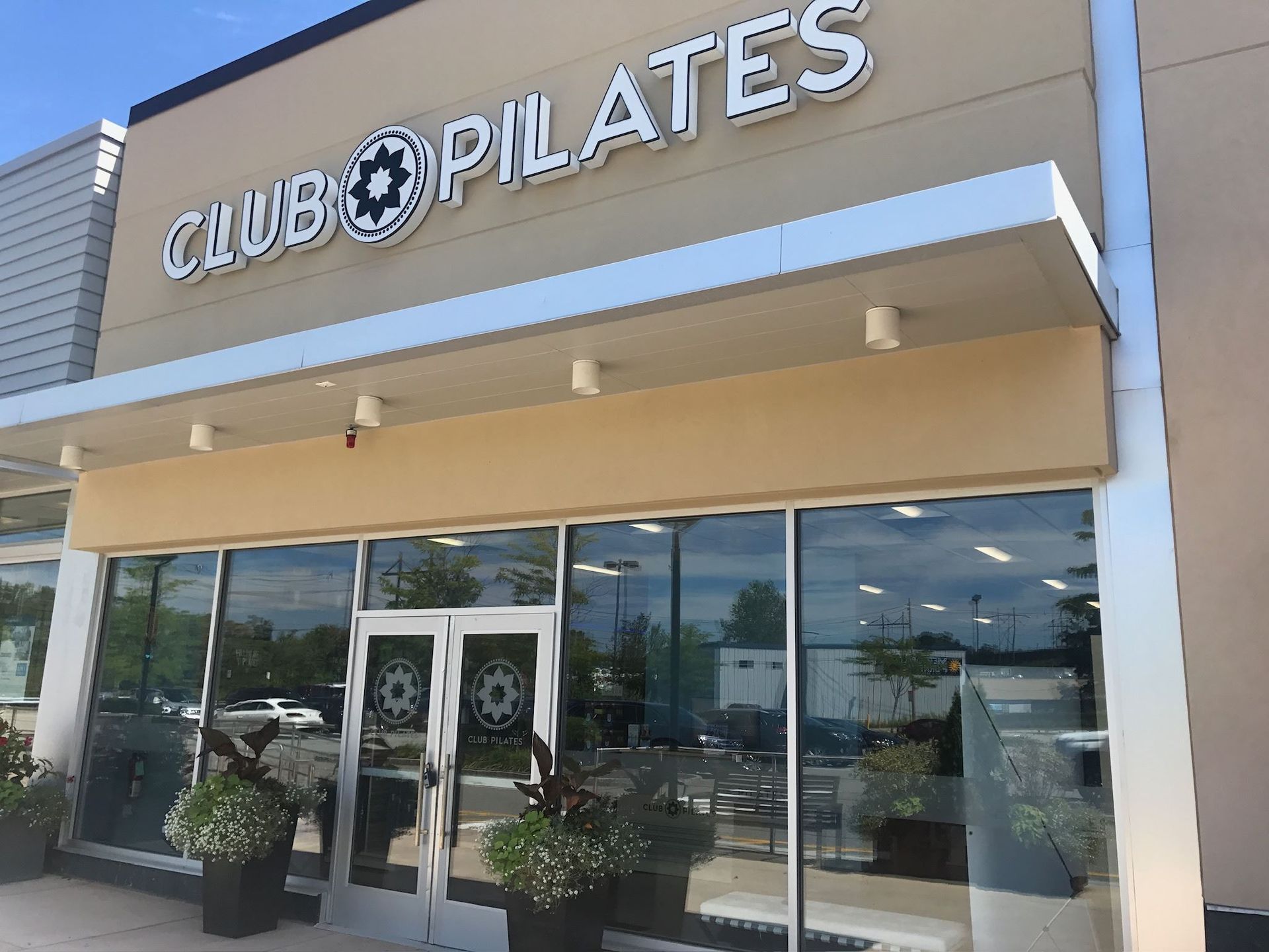 The front of a club pilates gym with lots of windows and plants in front of it.