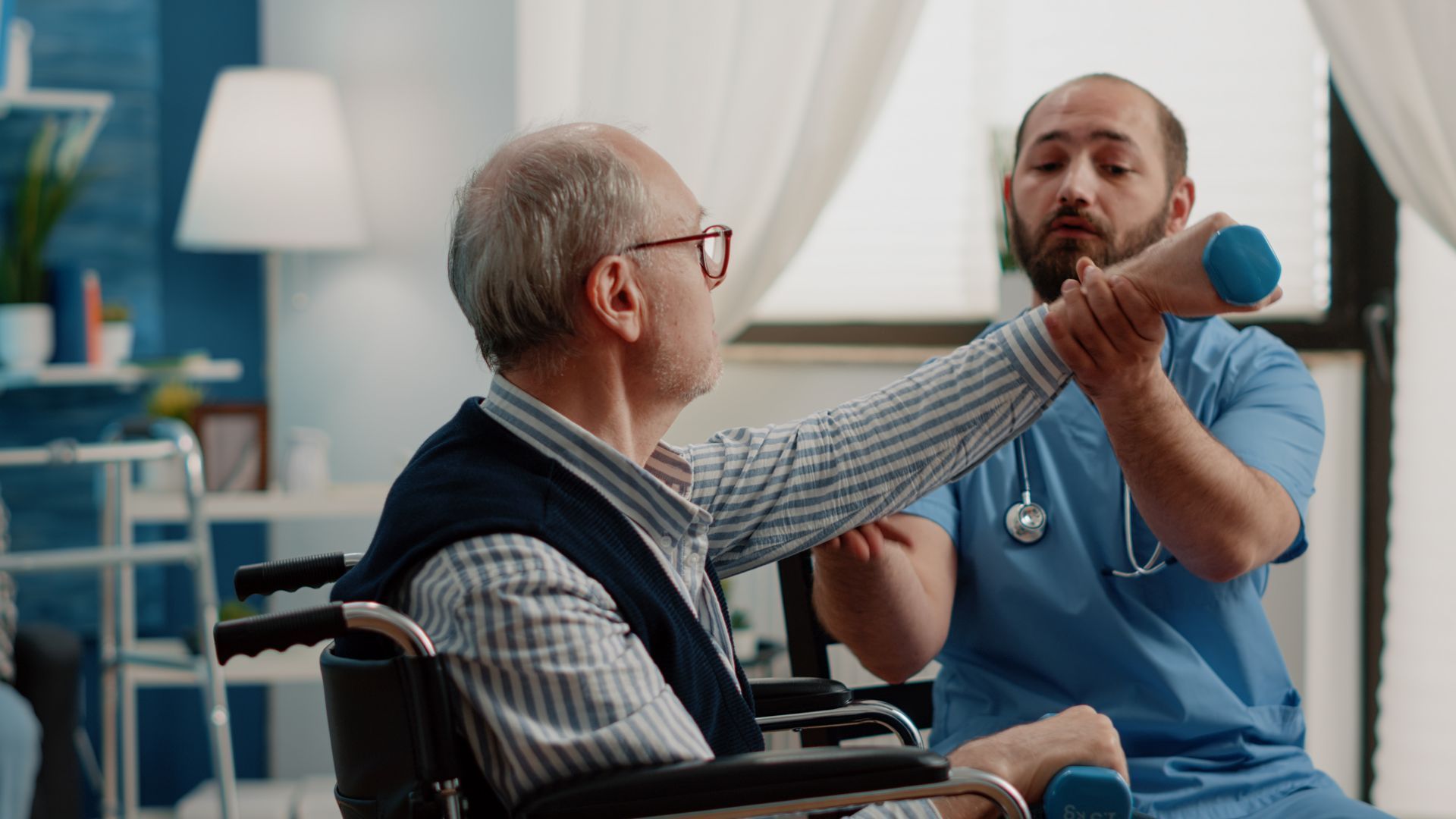 Physical therapist assisting elderly person in wheelchair with dumbbell exercise.