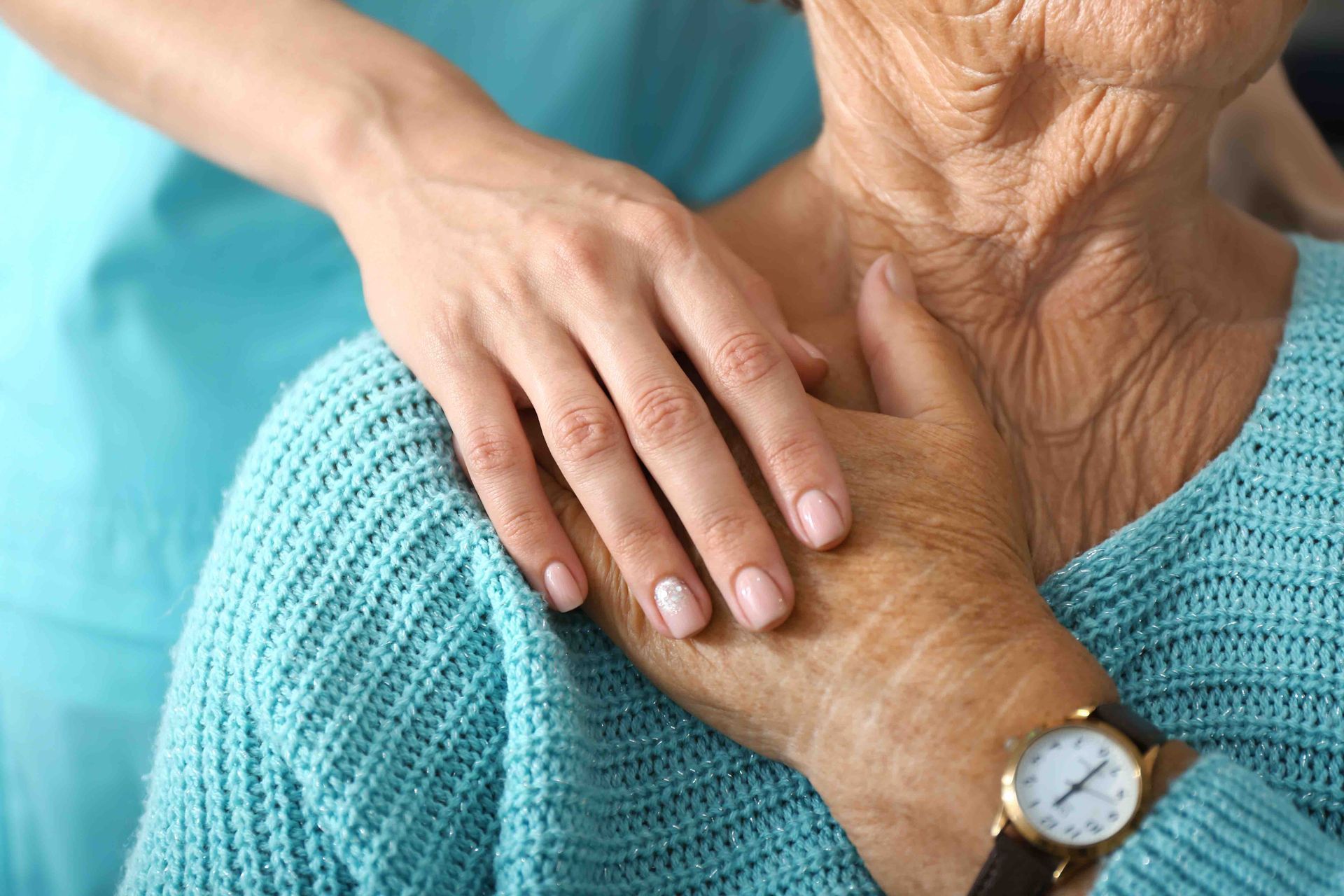 A person's hands supporting an older person's neck and shoulder. A watch is visible.