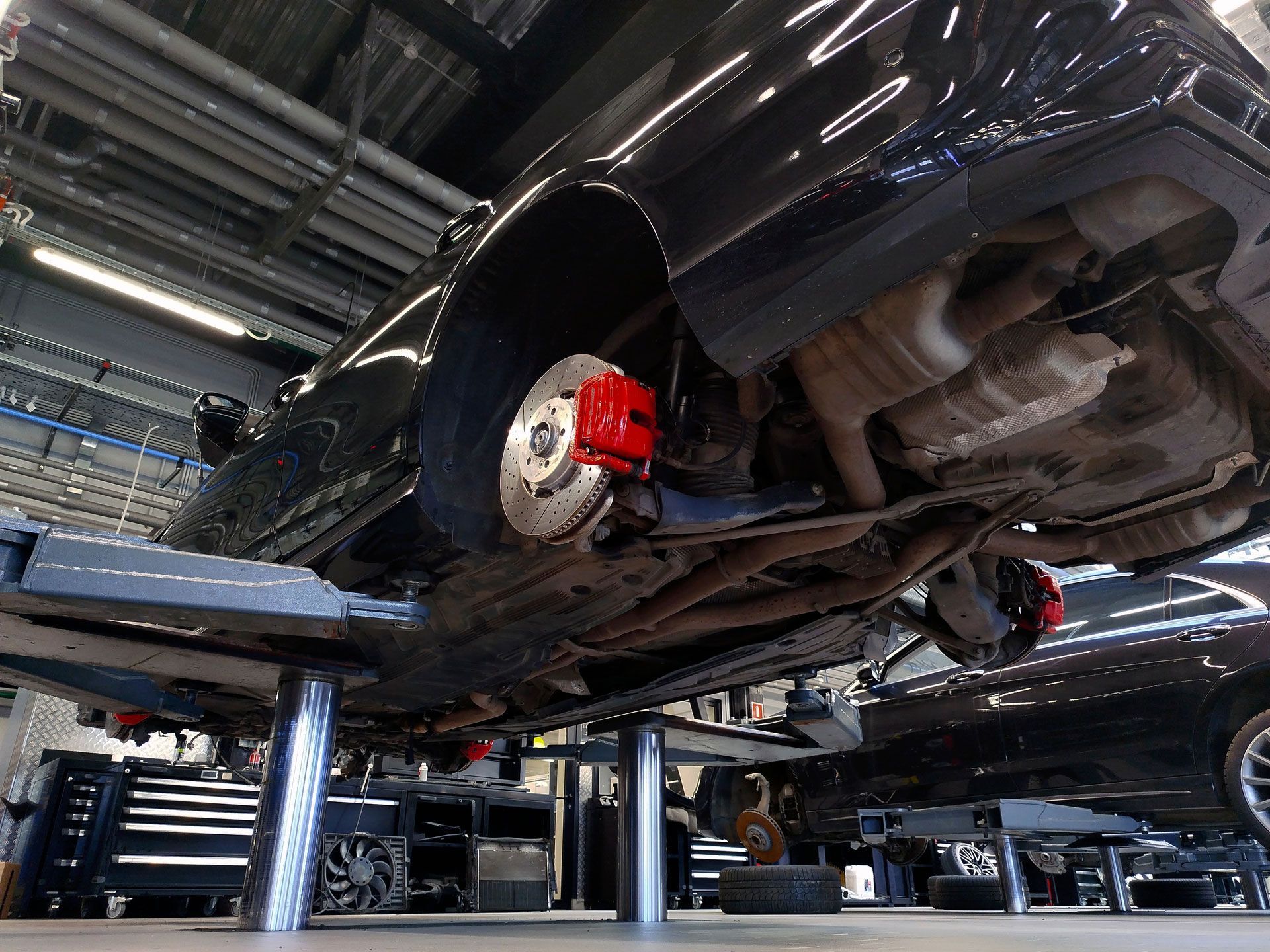 Black car raised on a lift in a garage, red brake calipers visible.