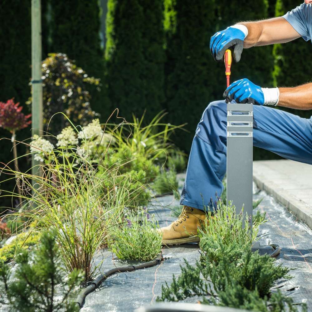 A man is kneeling down in a garden holding a screwdriver.