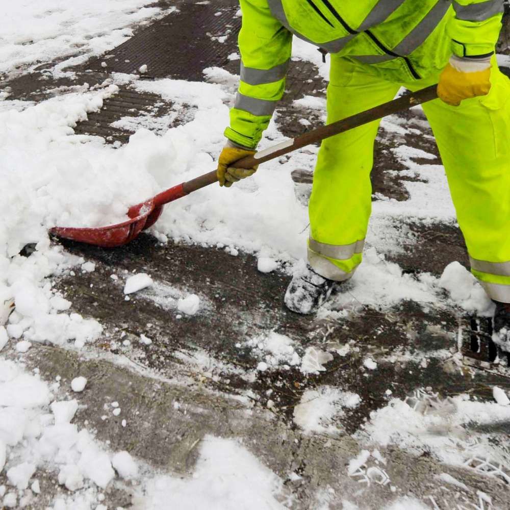 A person in yellow pants is shoveling snow with a red shovel.