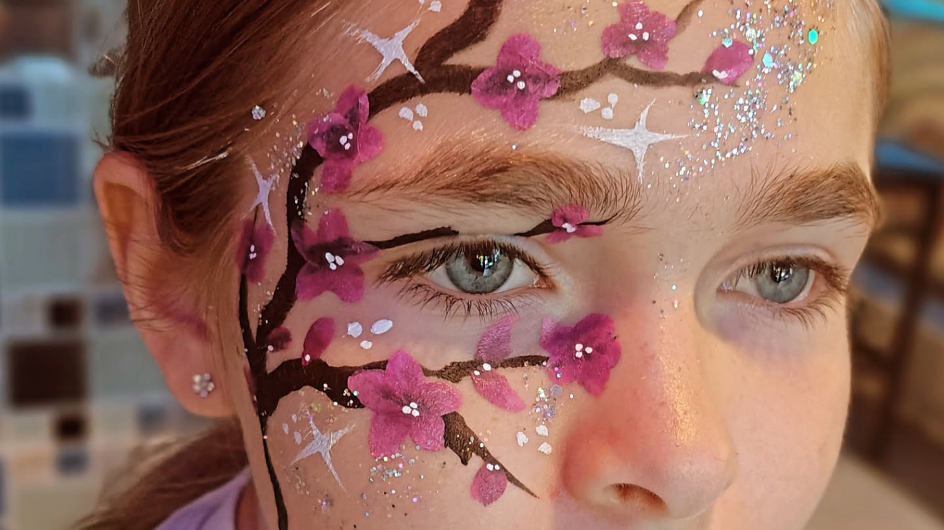 Girl's face with cherry blossom face paint. Dark branches, pink flowers, and silver glitter on the skin.
