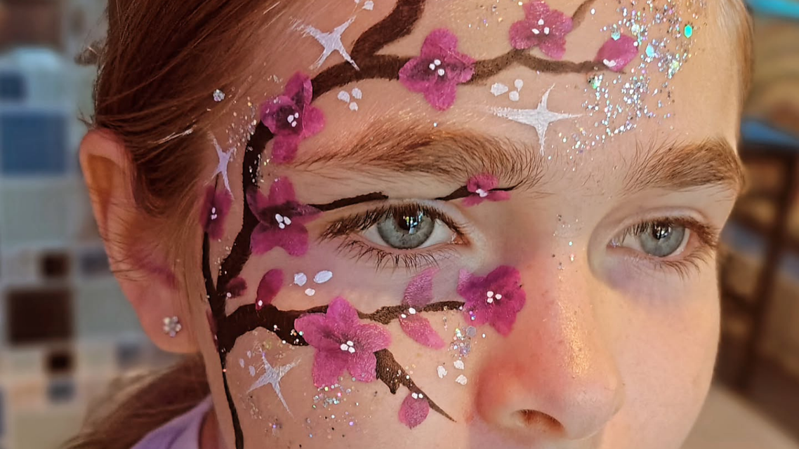 Girl's face with cherry blossom face paint. Dark branches, pink flowers, and silver glitter on the skin.