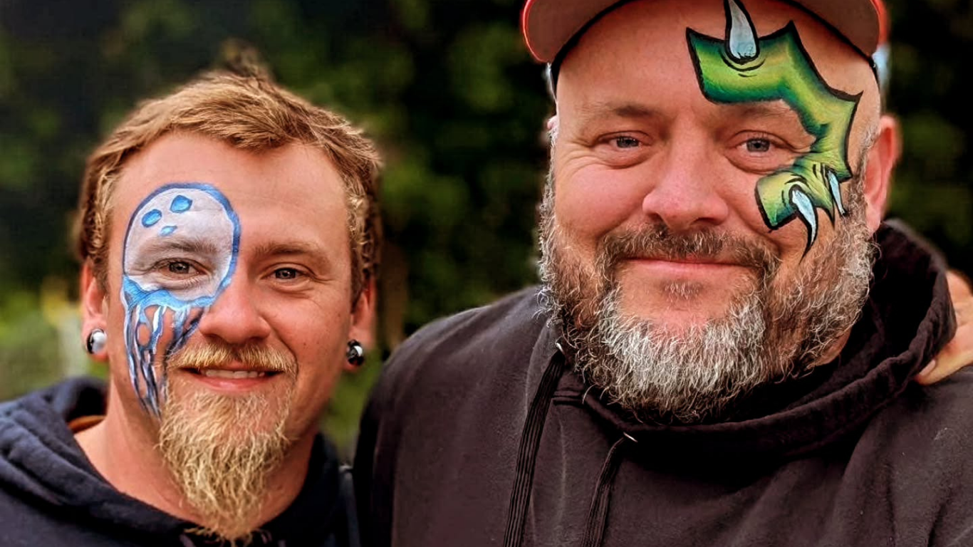 Two men with face paint, one as a sea creature, the other as a green dragon, smiling.