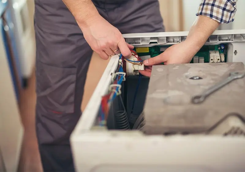 Un hombre está arreglando una lavadora con una llave.
