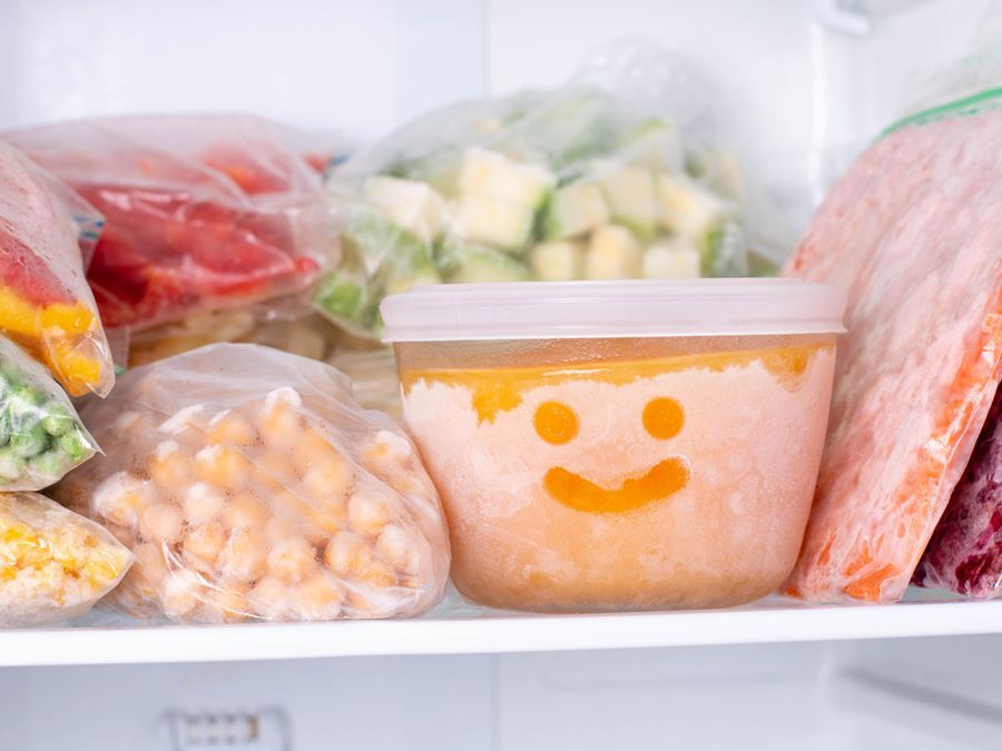 Un refrigerador lleno de verduras congeladas y un recipiente con una carita sonriente en él.