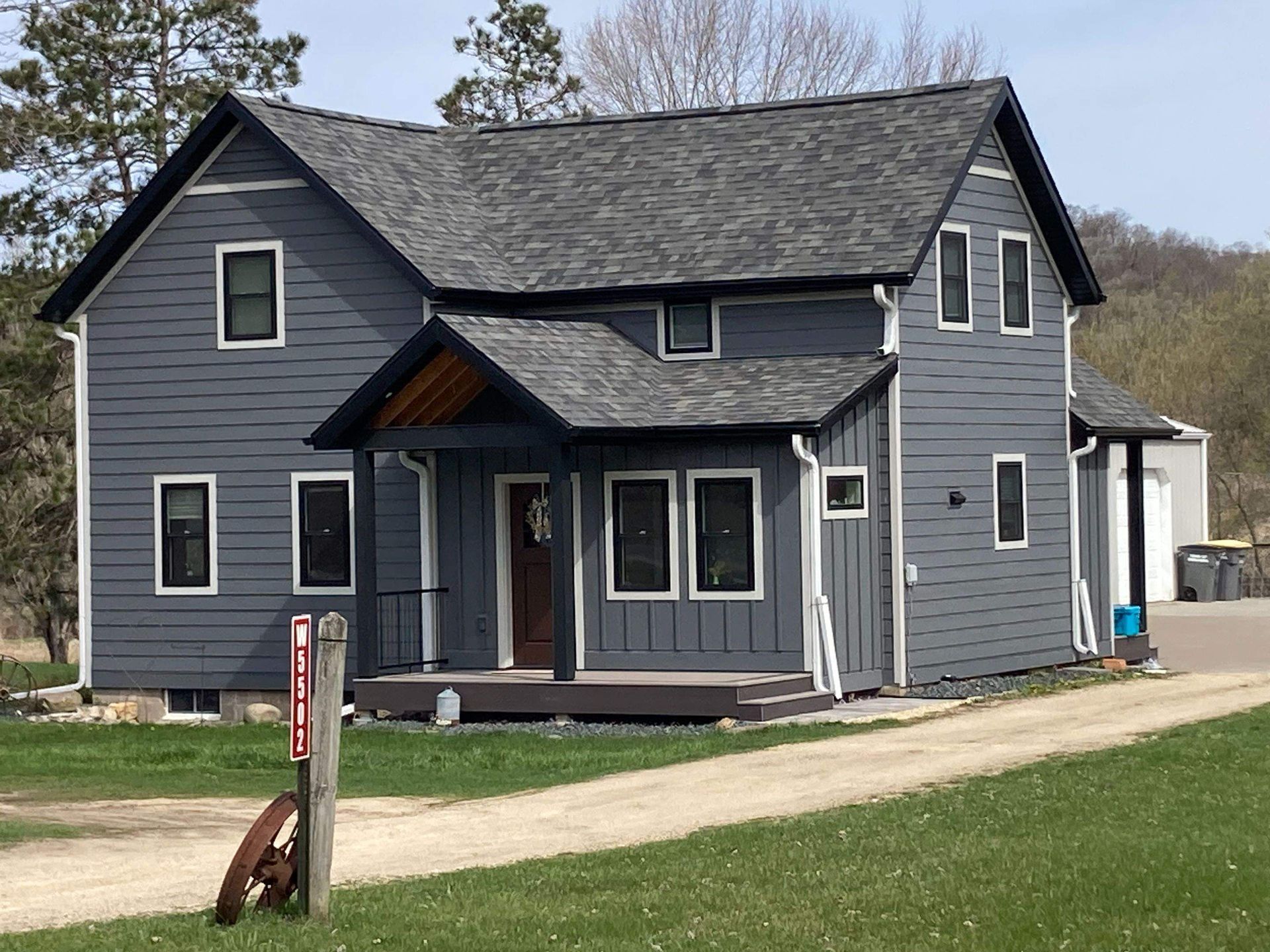 Gray farmhouse with black trim, porch, and a gravel driveway.