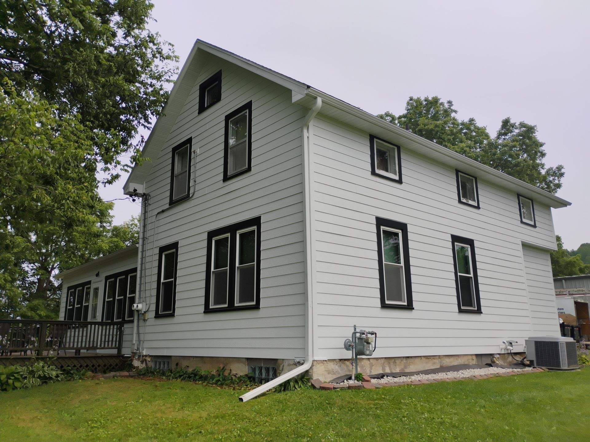 White two-story house with black window frames, green grass, and a cloudy sky.