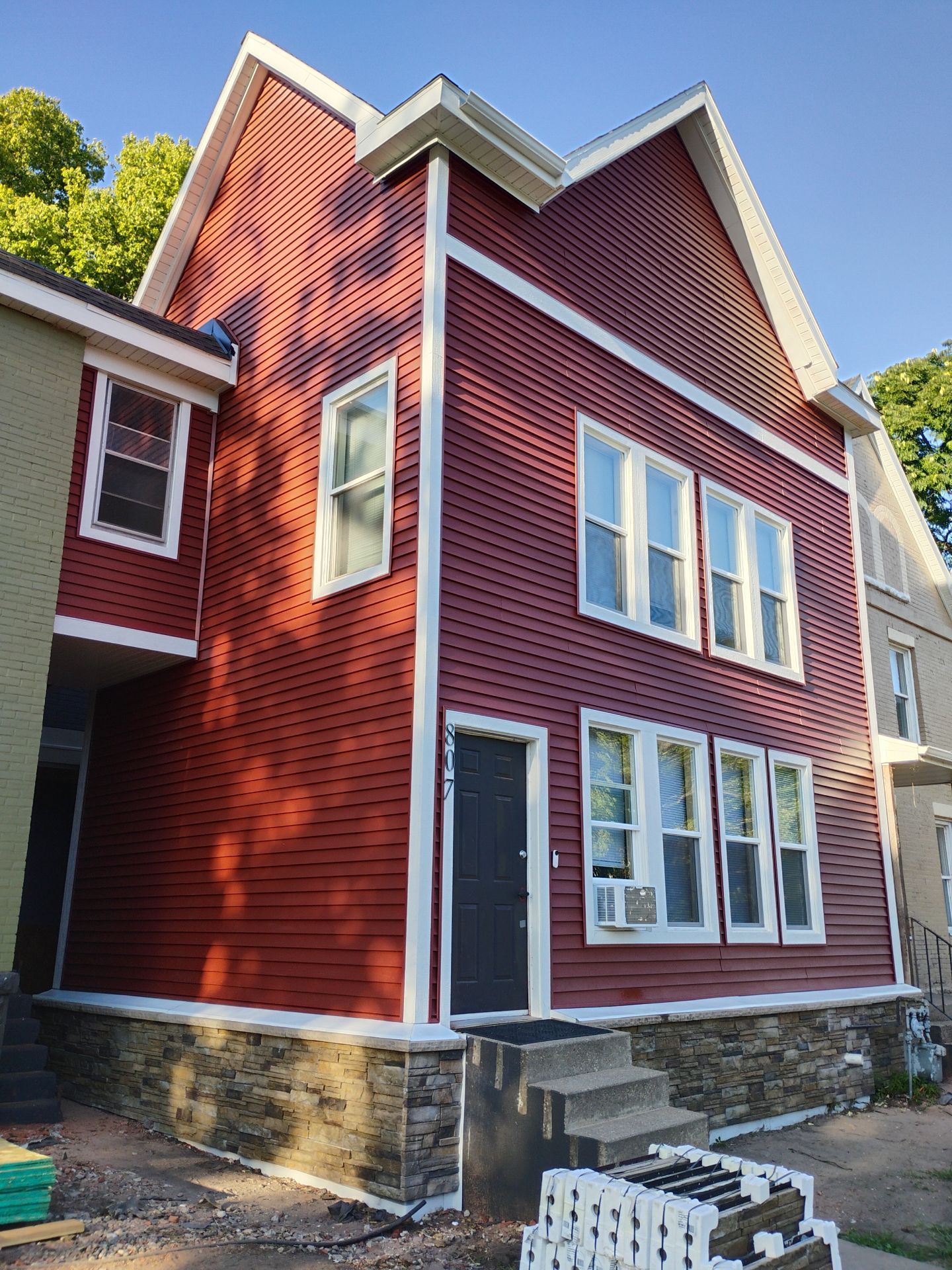 Red house with white trim, several windows, and a stone foundation.