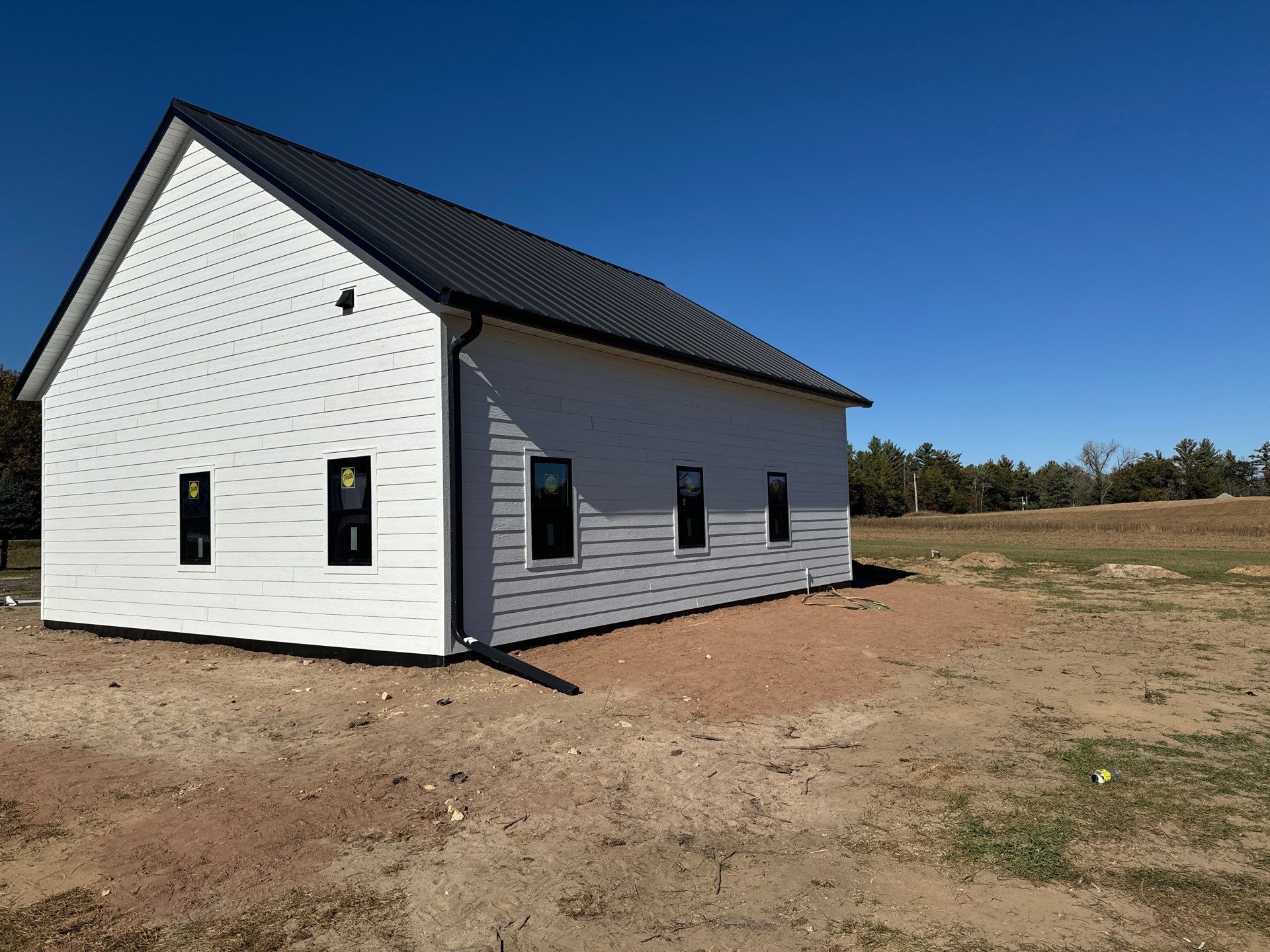 White house with a black roof and windows, on a dirt lot under a blue sky.
