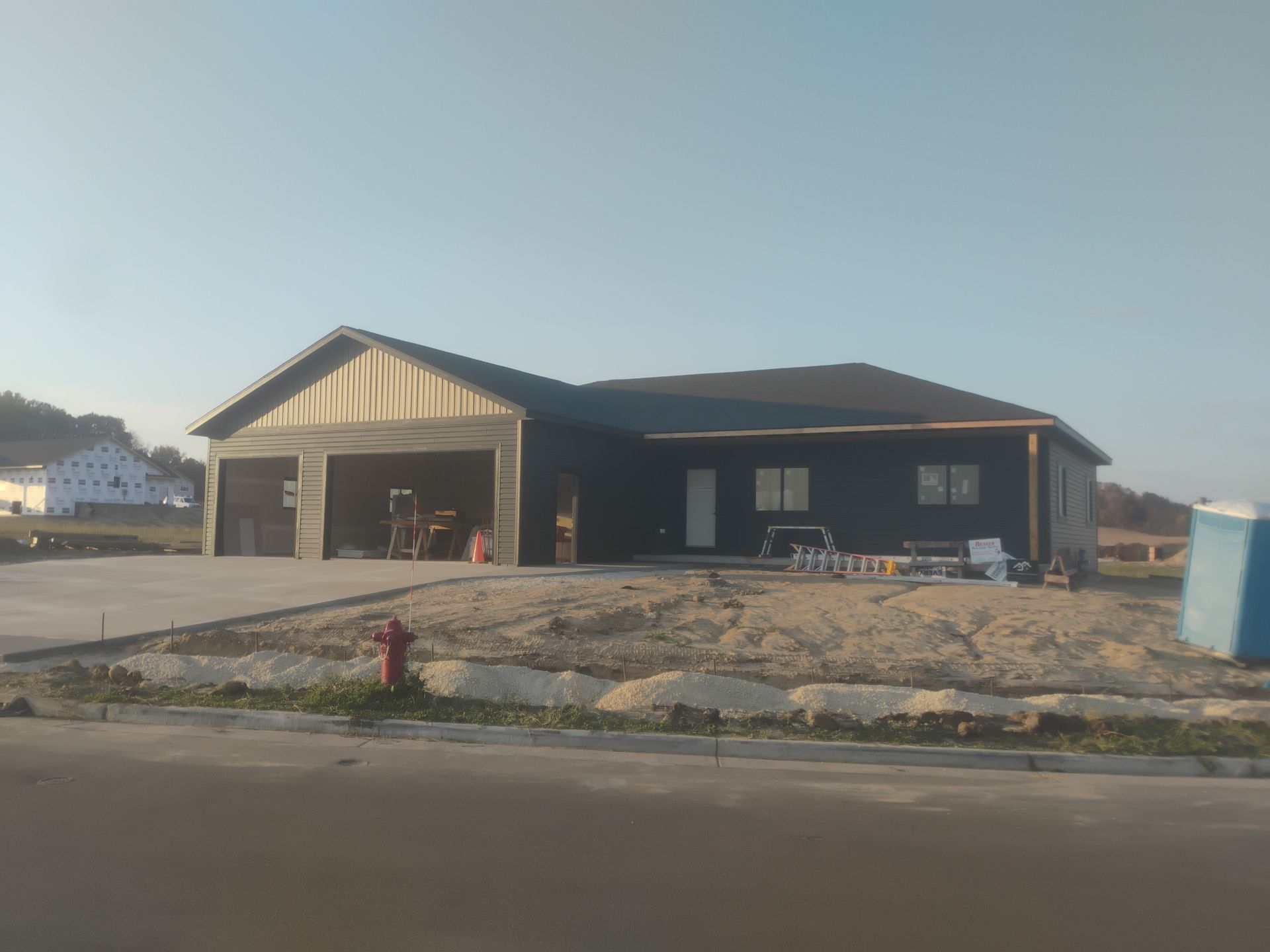 New construction home with dark siding, unfinished garage, and dirt yard.