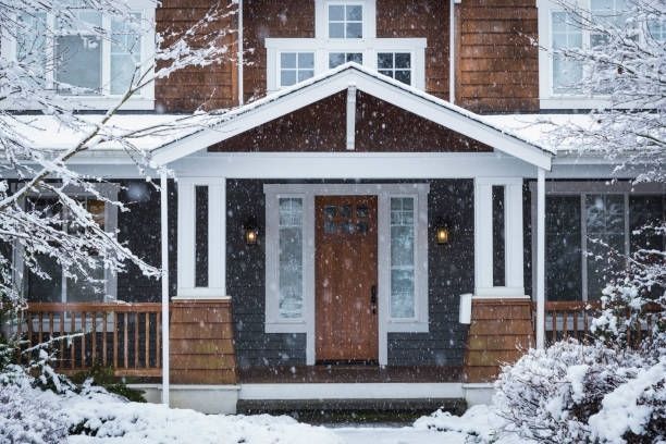 Snowy house exterior, dark siding and wooden porch, with snow falling.