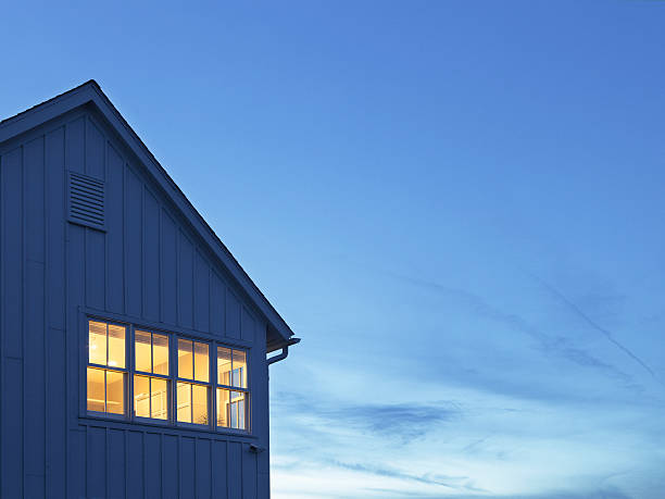 Blue house exterior with lit window against a blue sky at dusk.