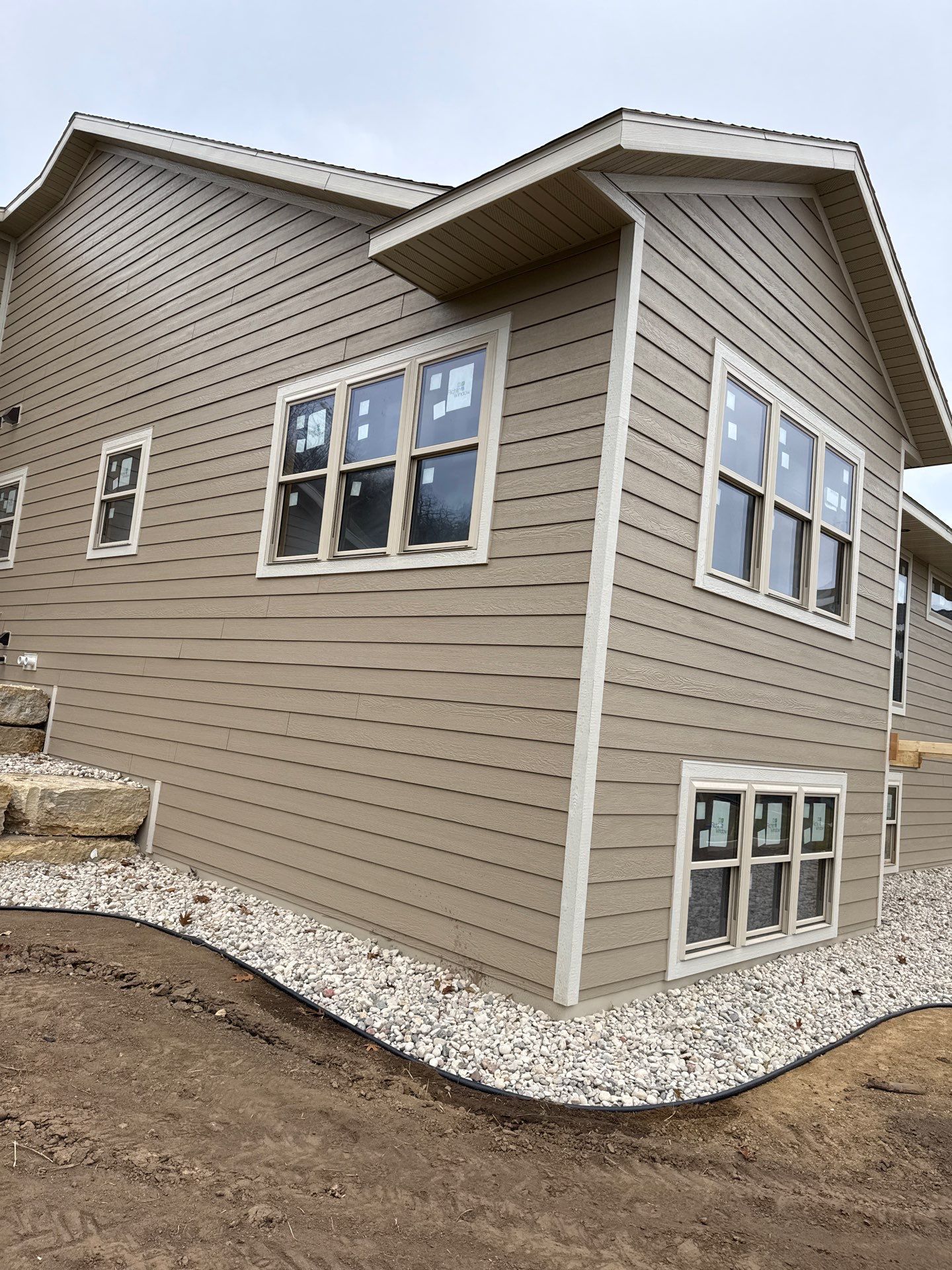 Beige house with light trim and windows, gravel border, overcast sky.