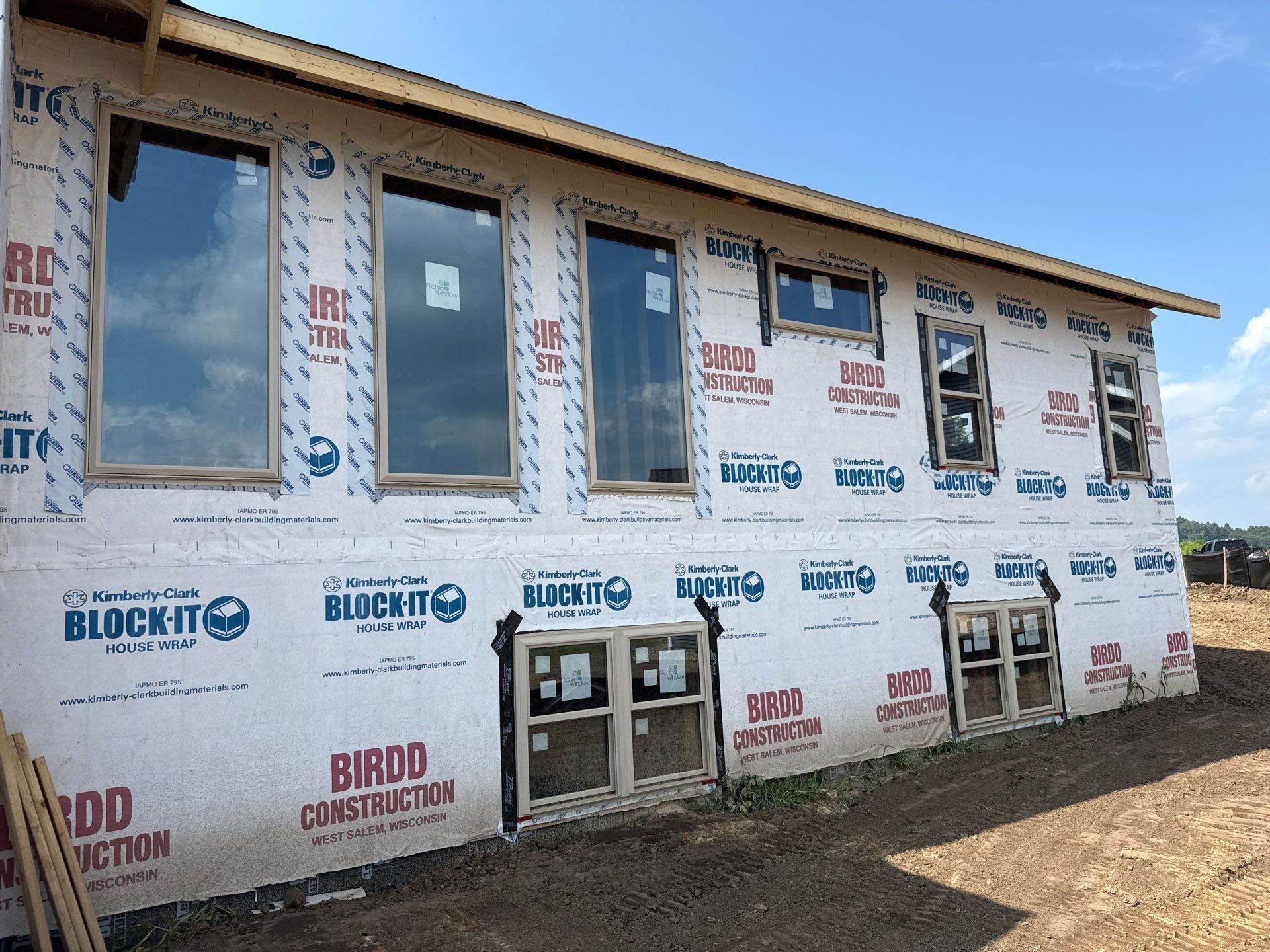Exterior of a building under construction, windows installed, covered in weatherproofing, on a sunny day.
