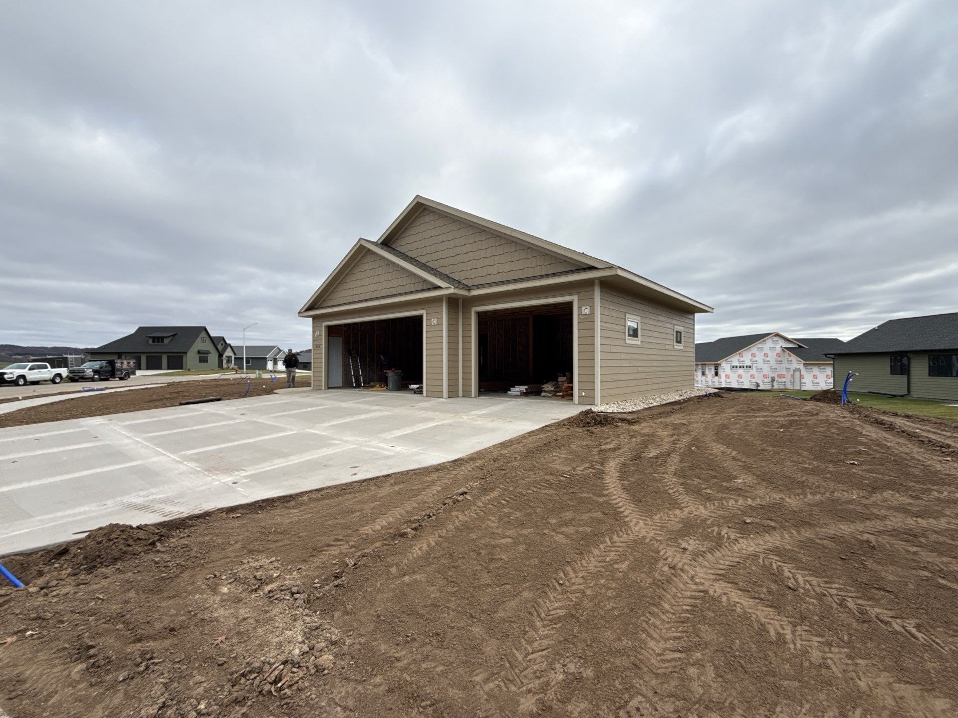 New two-car garage under construction with tan siding and concrete driveway in a suburban neighborhood.