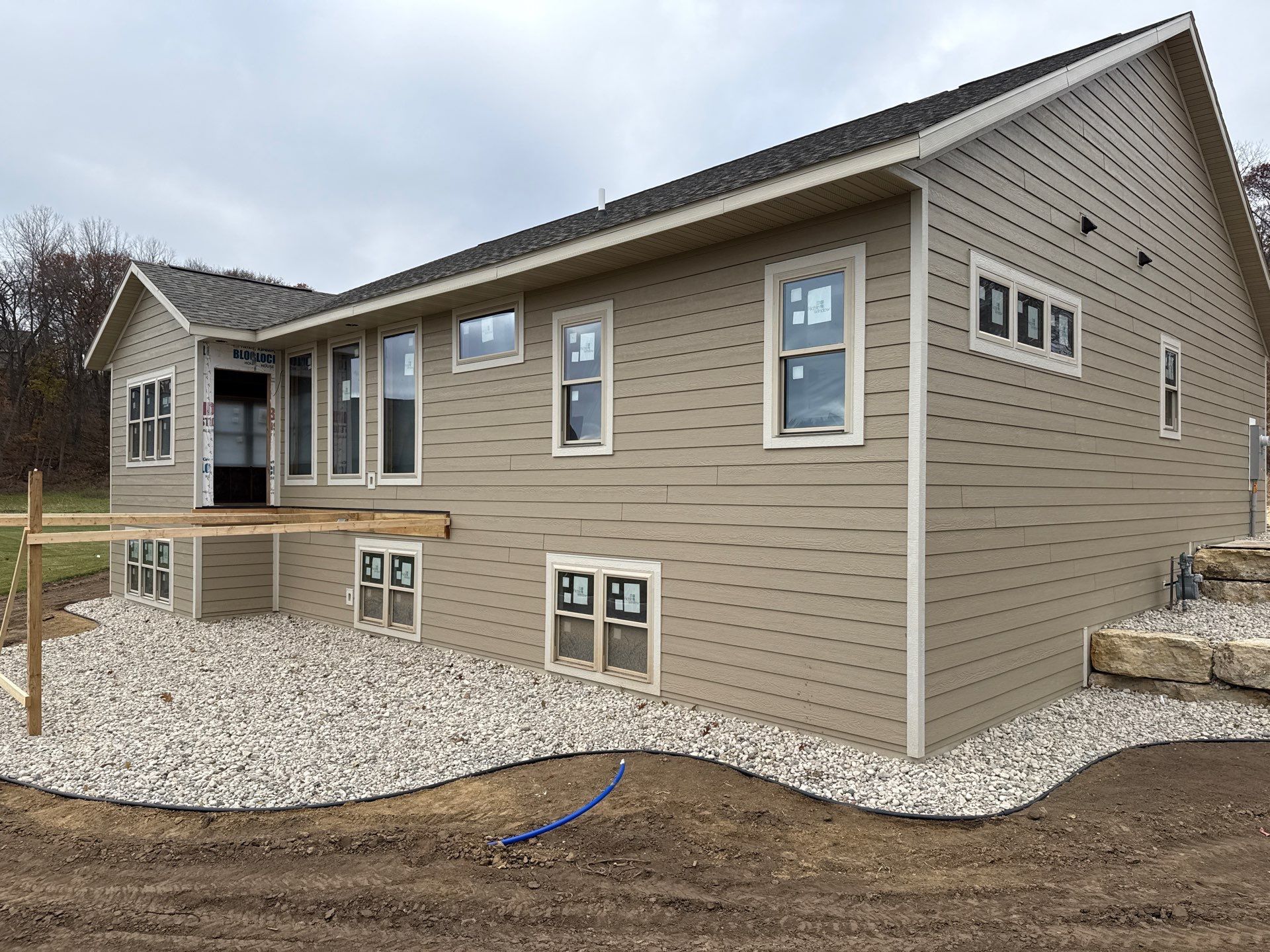 Beige house under construction, with light gravel landscaping and multiple windows.