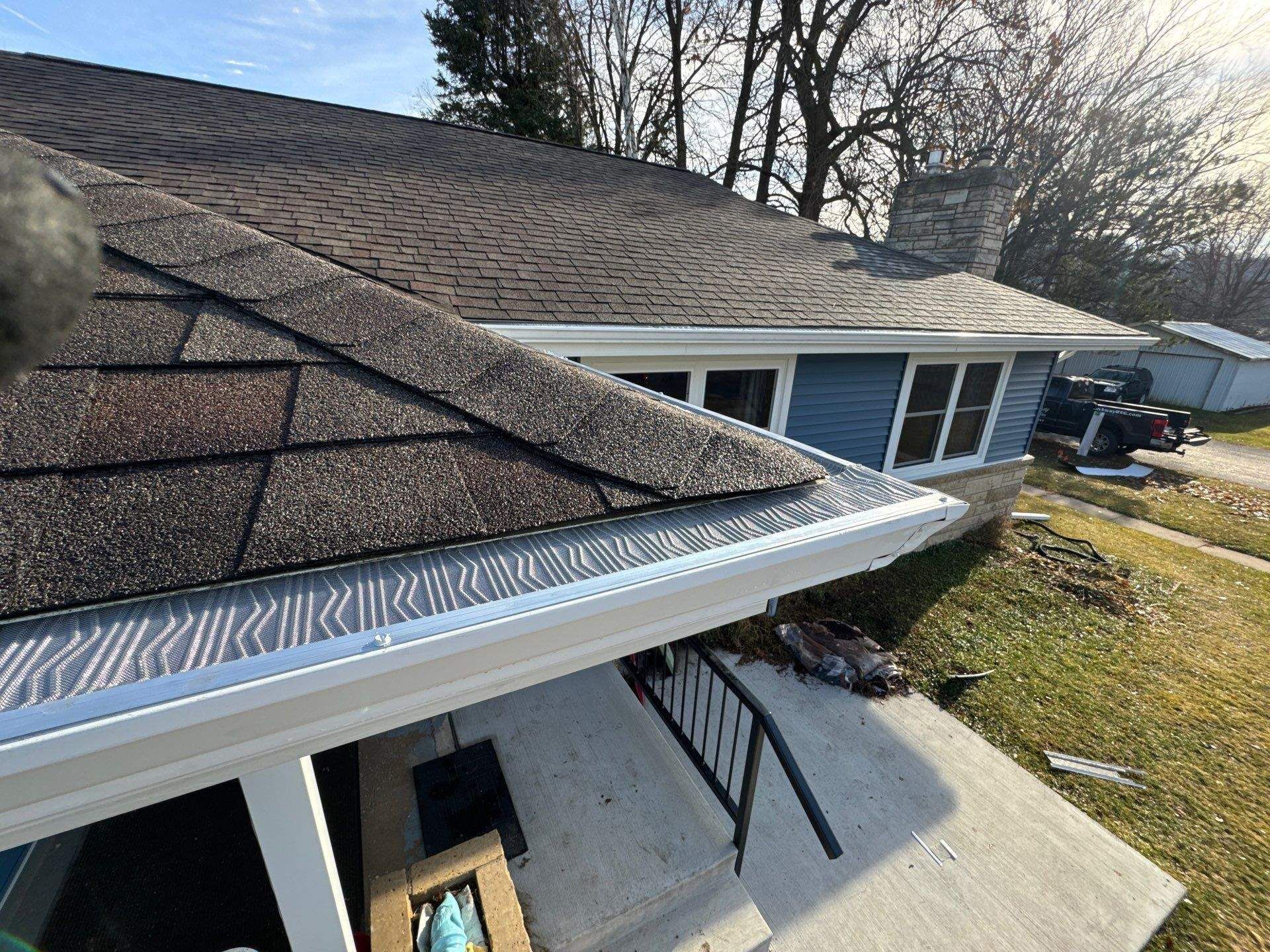 A house with a shingle roof and white gutters. Blue siding, a chimney, and a concrete porch are visible.