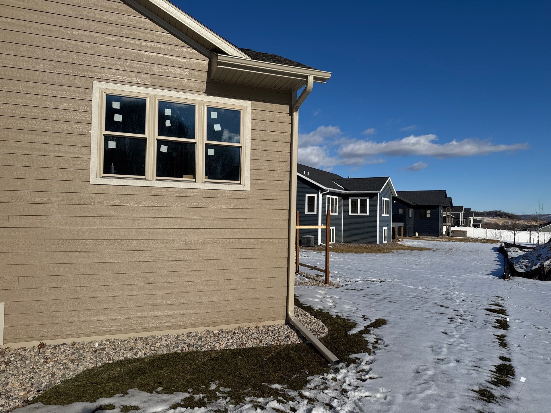 Tan house with window, row of dark blue houses, snowy ground, and blue sky.