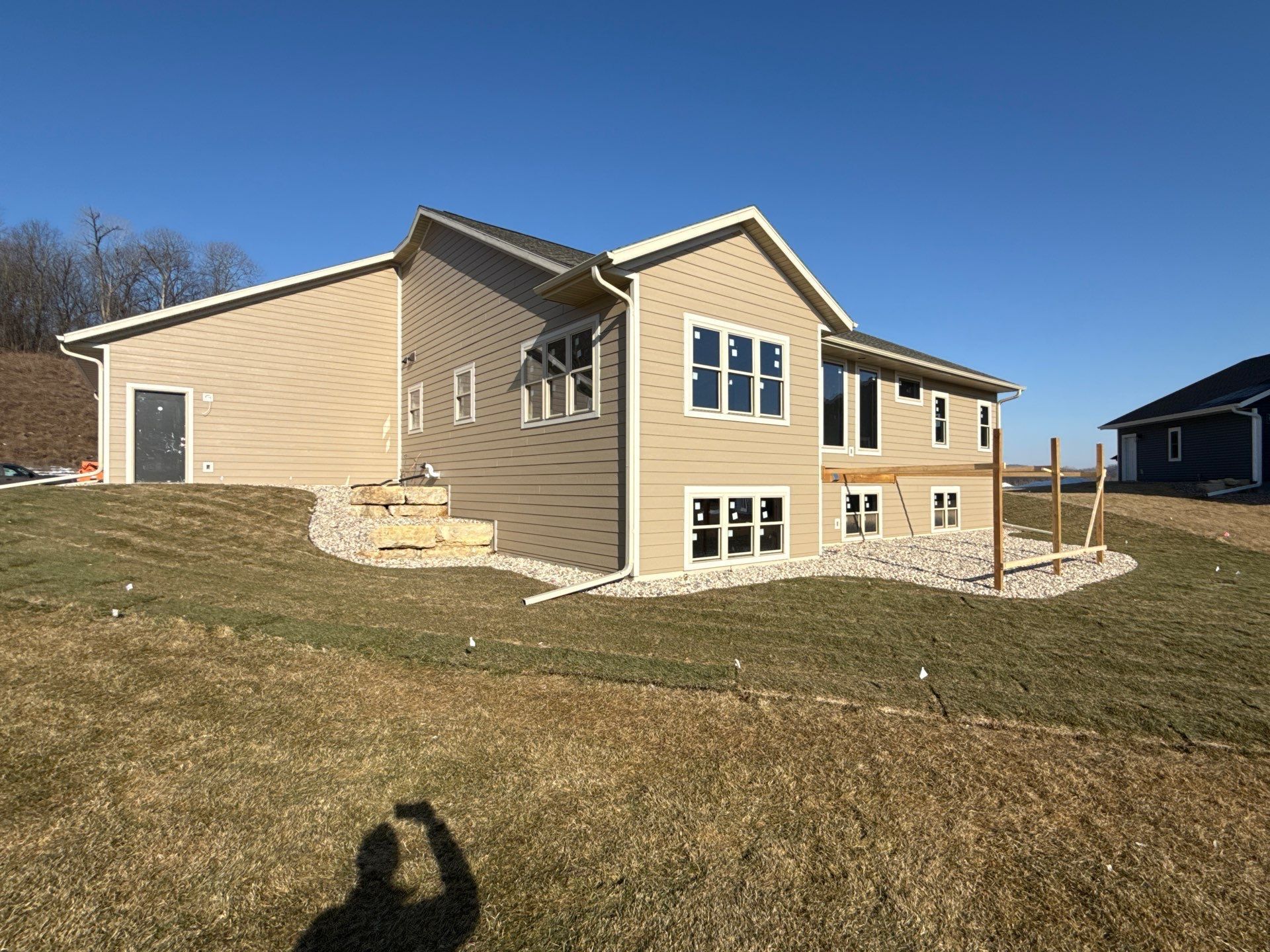 Beige house with large windows on a grassy hill under a blue sky; wooden posts on a patio.