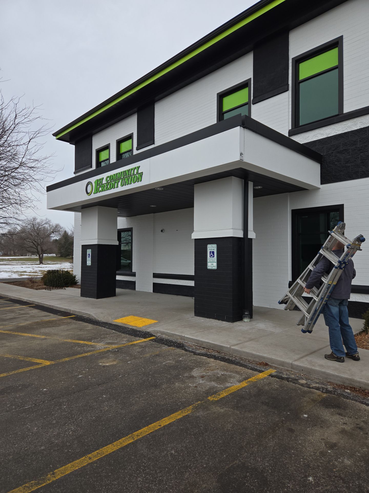 Person carrying a ladder near a two-story brick building with a green and black facade.
