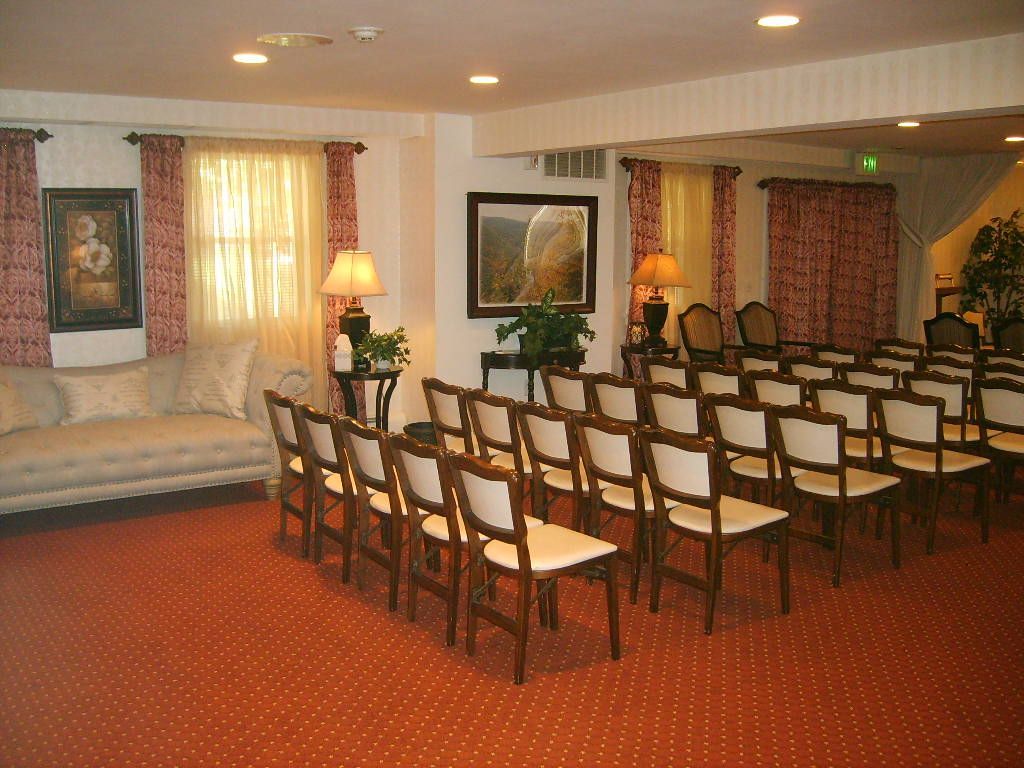 A viewing room set up with chairs for a memorial service; red carpet and drapes.