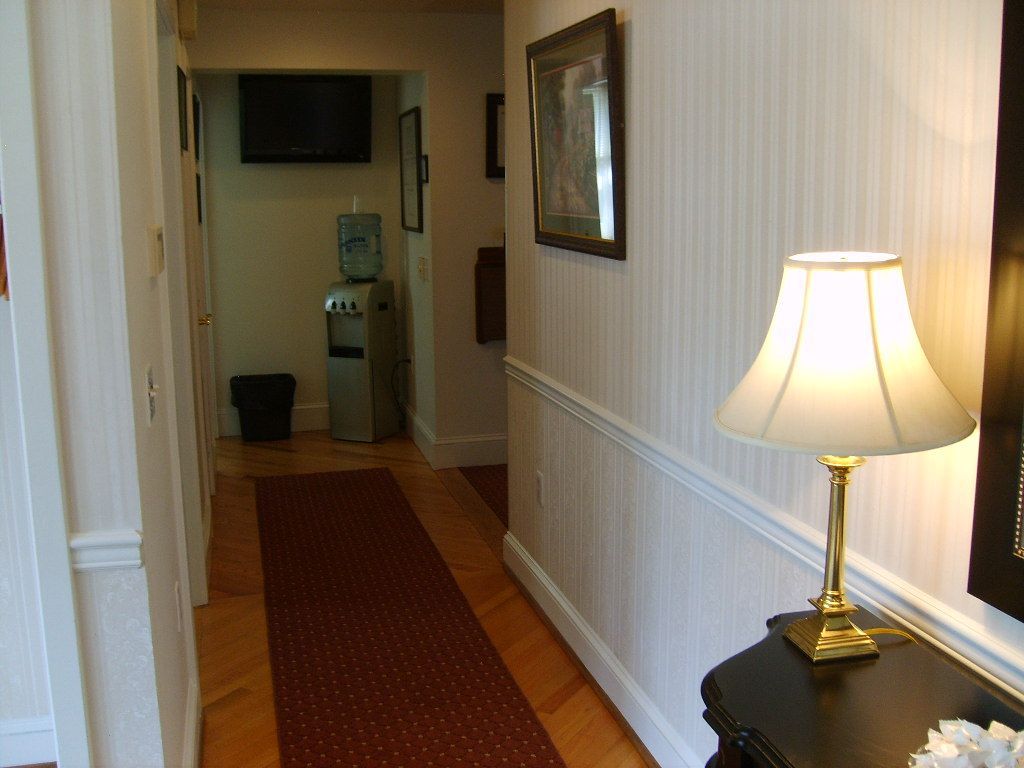 Hallway with red runner, lamp on table, water cooler, and artwork on walls.