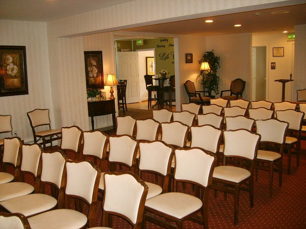 Rows of cream-cushioned chairs face an open doorway in a room with patterned walls, a formal setting.