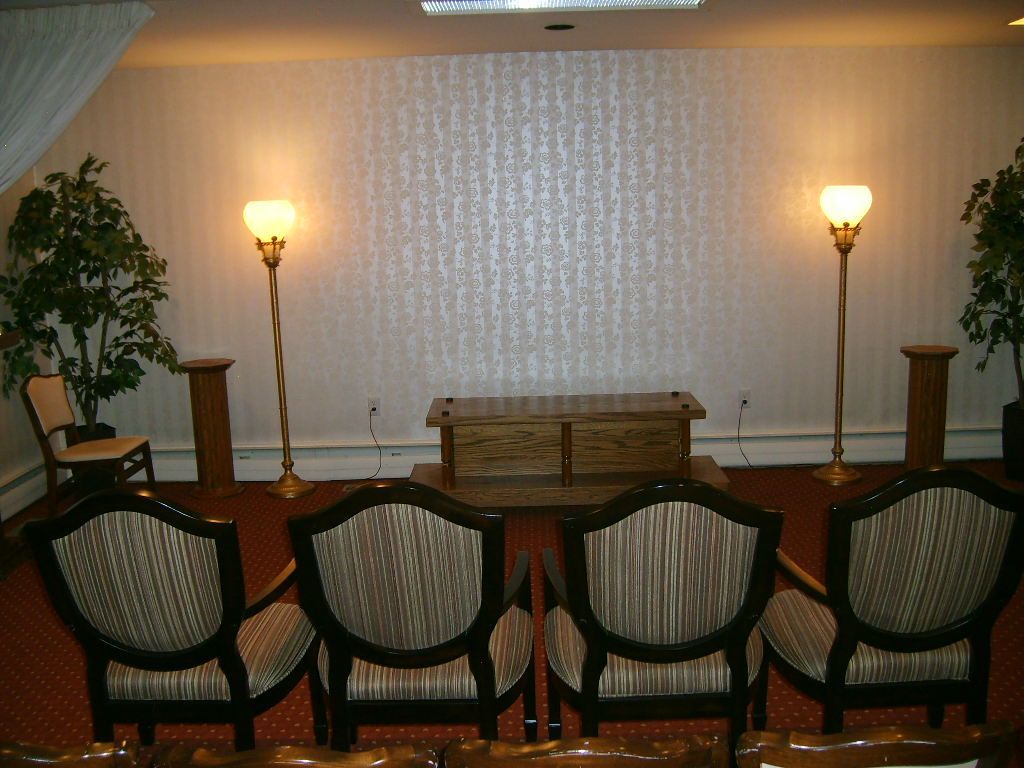 Funeral home interior with chairs facing a wooden casket and two lamps.
