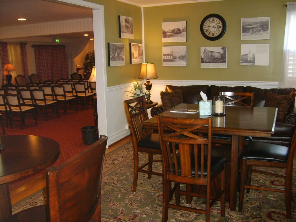 A room with tables, chairs, a sofa, and a doorway to a seating area. Green walls, rug, and black and white photos.