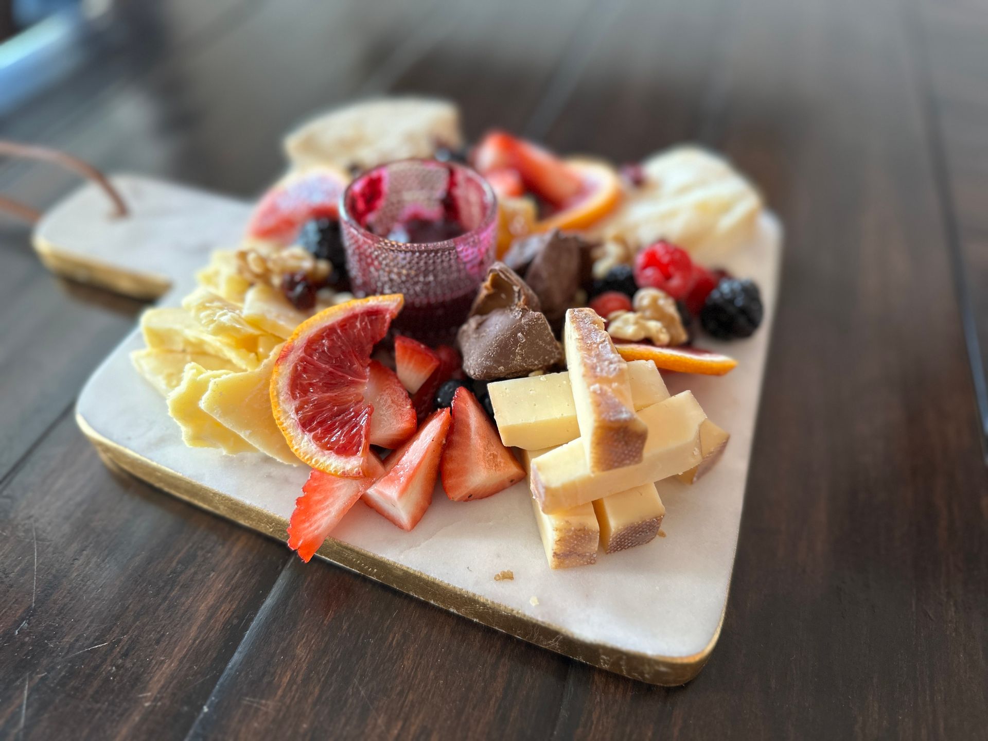 A wooden table topped with a cutting board filled with cheese , fruit and nuts.