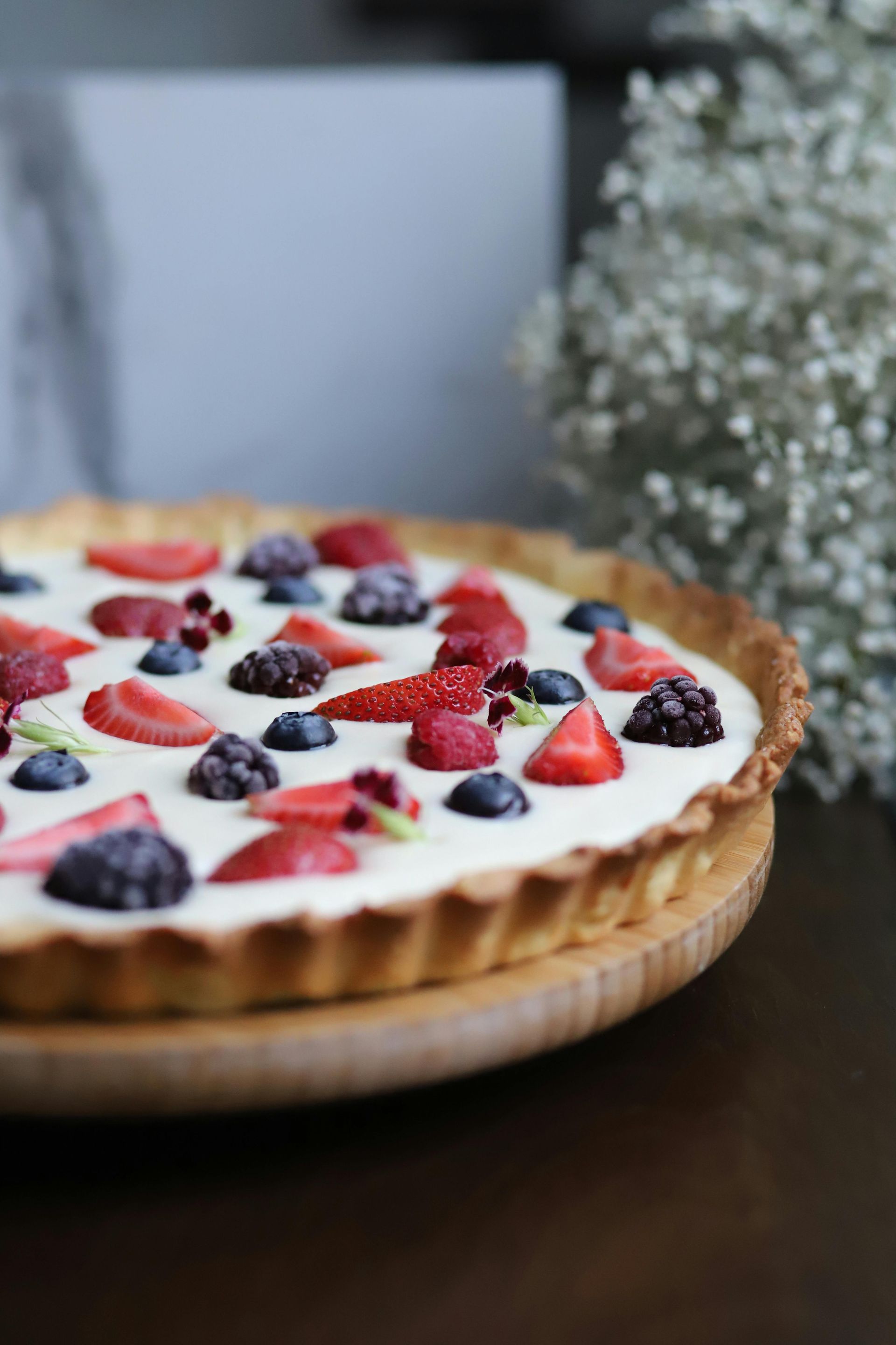 A pie with strawberries , blueberries , blackberries and whipped cream on a wooden plate.
