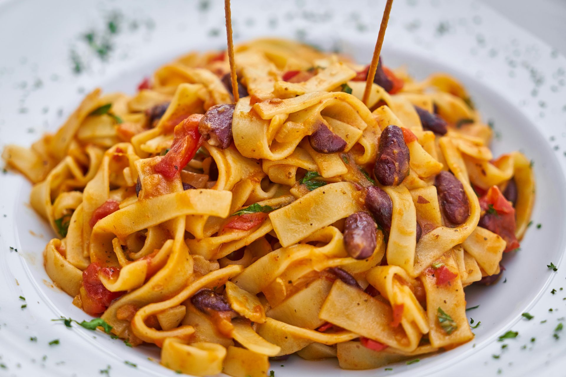 A close up of a plate of pasta with beans and tomatoes