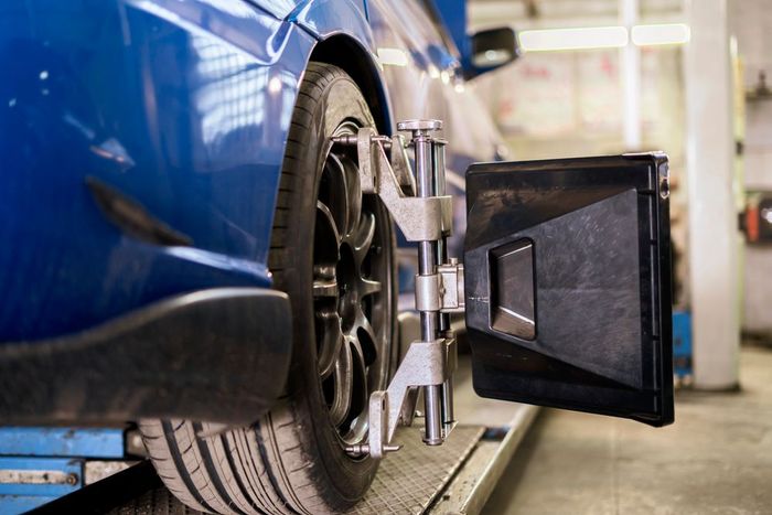Pneumatico blu per auto su un ponte sollevatore, sottoposto a convergenza. Attrezzatura nera e argento fissata alla ruota.