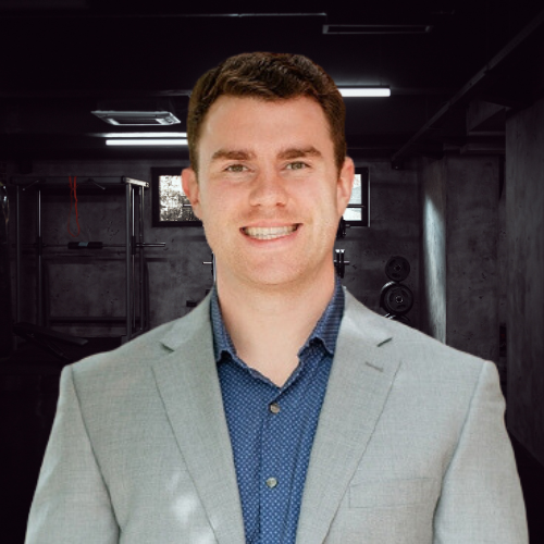 Man in a suit smiles in front of a dim gym.
