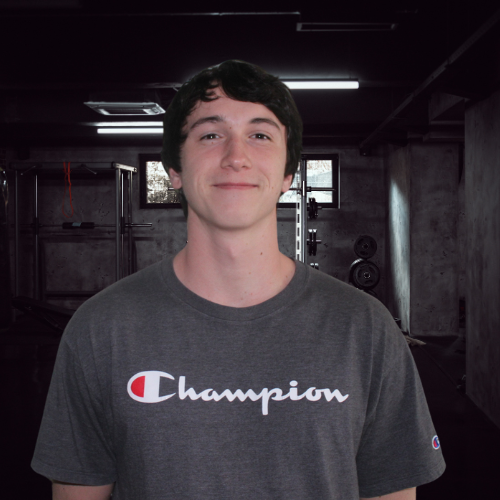 Man in gray Champion shirt smiles in a gym setting.